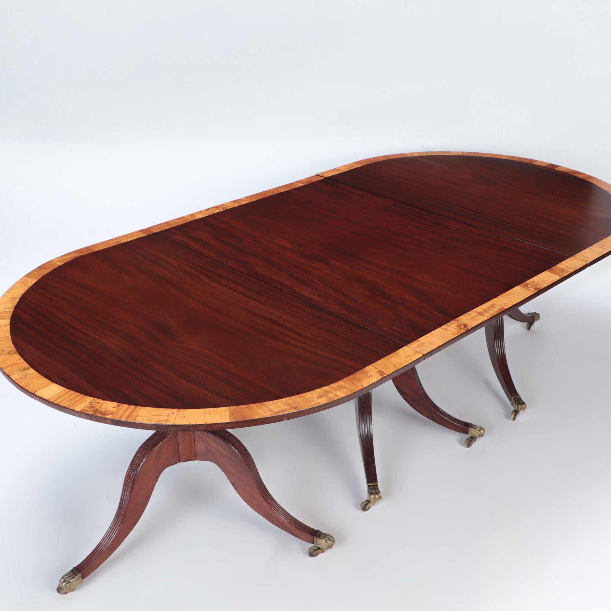 A Mahogany triple pedestal dining table with banded top. Reeded legs, nine brass paws with casters. England, circa 1910.
Two leaves. Each is 21.75