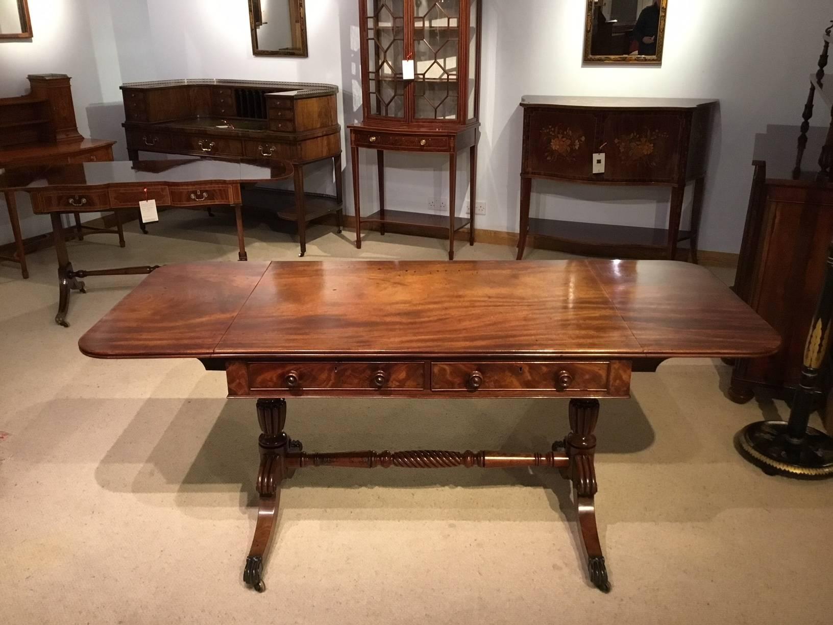 A mahogany William IV period antique sofa table. Having a rectangular solid Cuban mahogany top with twin drop leaves and a reeded edge above two mahogany lined frieze drawers with flame mahogany drawer fronts, turned mahogany drawer pulls and dummy