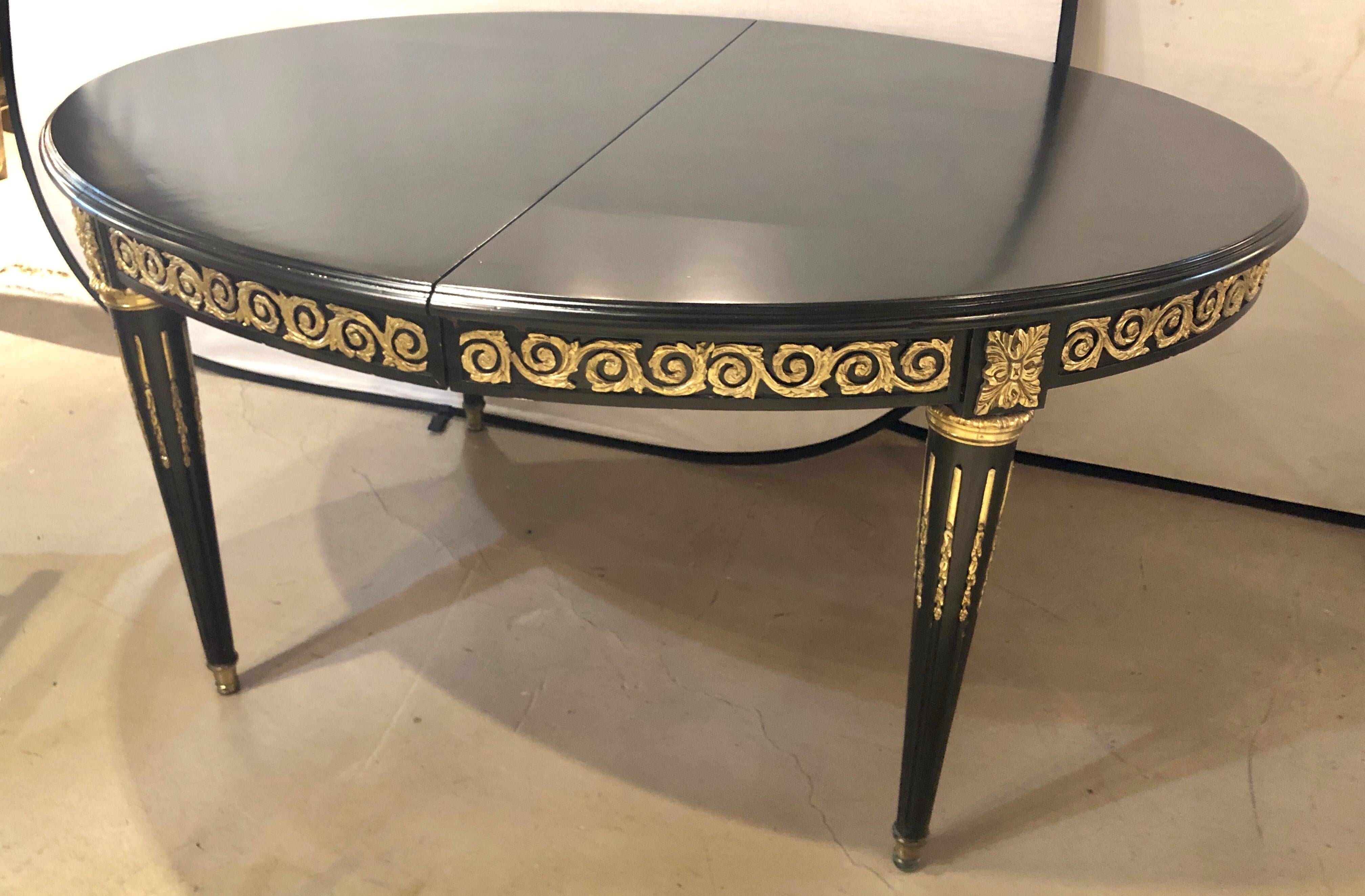 A Hollywood Regency Louis XVI style heavily bronze mounted dining table having one 24 inch Leaf in an ebony finish. The tapering bronze mounted and fluted legs leading to cookie cutter corners with bronze swirl mounts on the apron. The oval tabletop