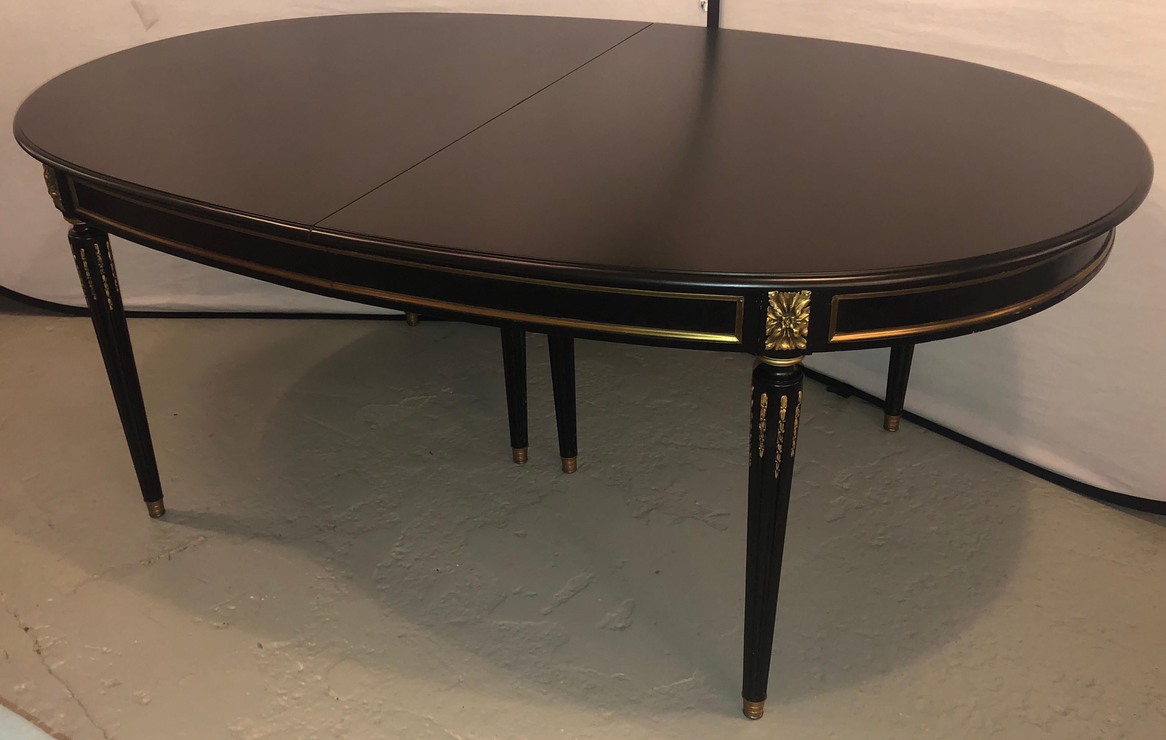 Louis XVI style refinished ebony dining table with two leaves measuring 20 inches each. This stunning Hollywood Regency dining table is simply stunning. The tapering Louis XVI Style bronze mounted legs with flame inserts on the reeded centre legs