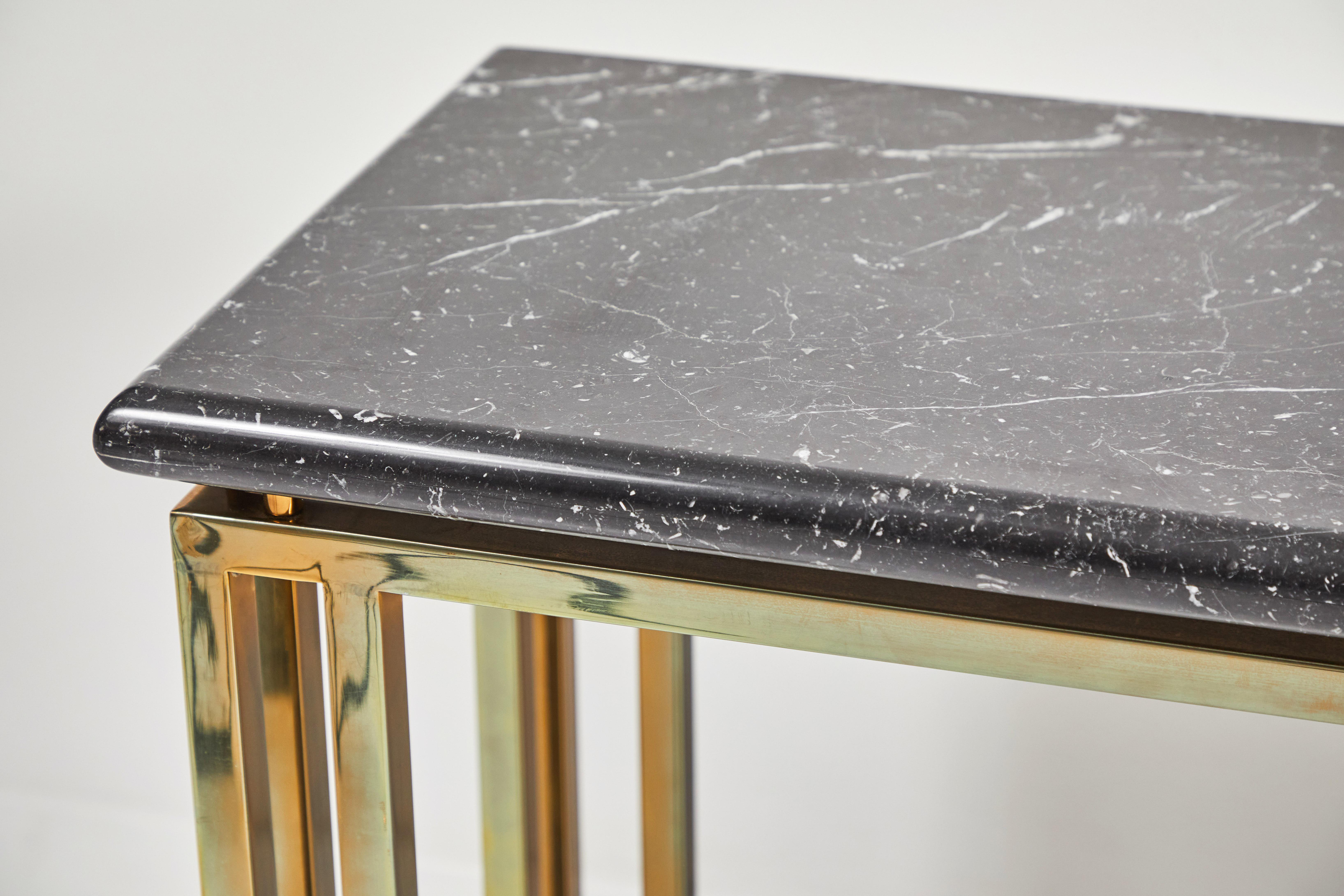 Sleek and stylish, this console top is a beautiful black Marquina marble with thin white veining. The top rests on 8 brass fittings that are secured to the base. The base is a polished brass and all one piece. The four legs are designed with 3