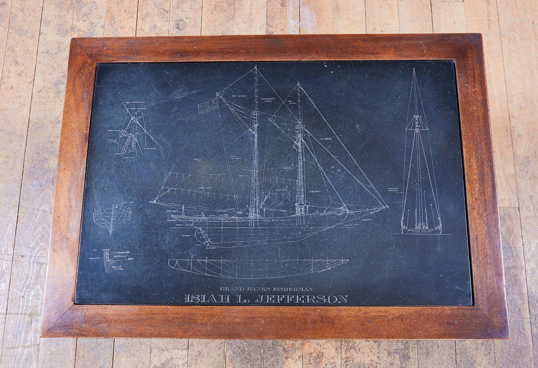 A maritime slate top drinks table in mahogany with turned X-stretcher base featuring a bordered slate top with a detailed etching of a two masted working yacht and marine architectural sketches. Small dimensions suitable for a drinks table next to a