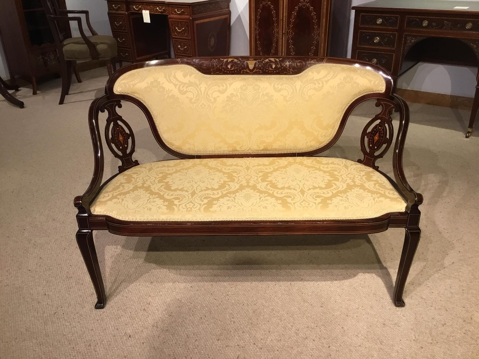 A marquetry inlaid Edwardian period antique settee. Having a curved back with a fine marquetry and pen-work inlaid panel above the central padded back, flanked by pierced fretwork panels, with open arms and padded seat. Supported on slender cabriole