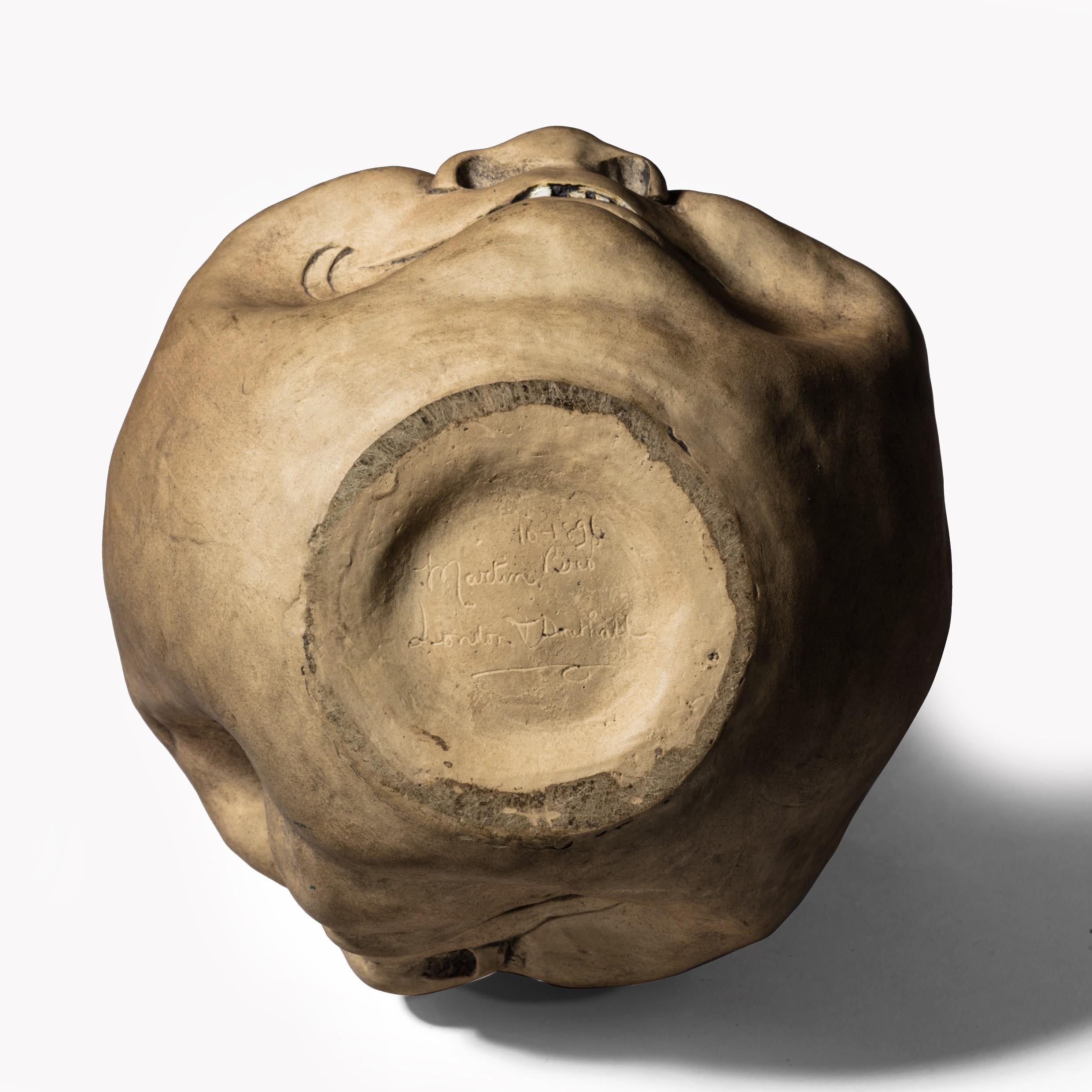 A Martinware double-sided stoneware pottery ‘face’ jug, dated 1896, of asymmetrical globular shape with a single handle, incised and salt-glazed on each side with a grinning face, one winking, the interior and handle glazed, signed ’10 1896, Martin