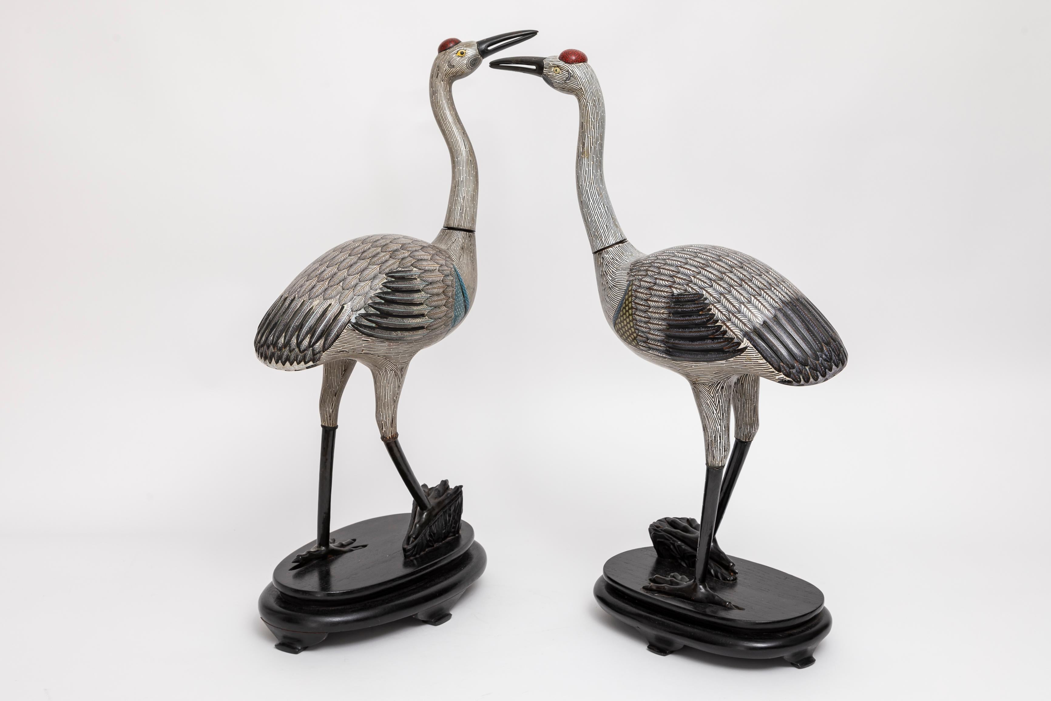 A Marvelous and Large Pair of Chinese Cloisonné Figures of Cranes on Stands.  Step into the captivating world of Chinese artistry with this remarkable pair of cloisonné figures of cranes, hailing from the Qing Dynasty.  The red-crowned crane holds a