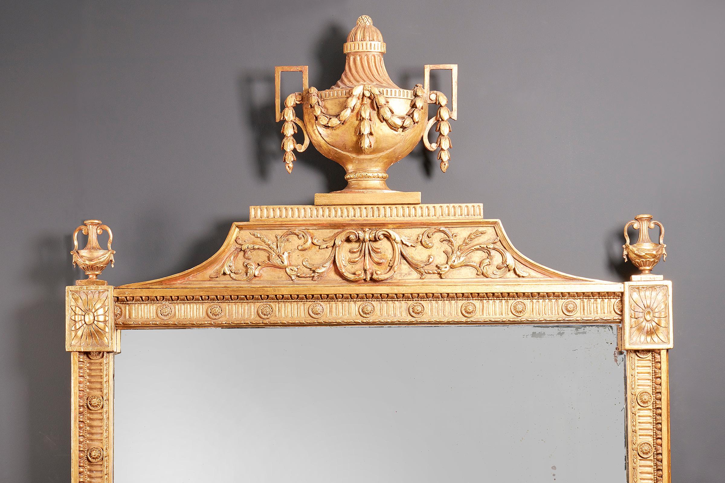 A fine George III gilt wood mirror, circa 1775-1800, of grand size, the frame with a flower head in each corner, the upper corners surmounted by classical urns, the top with a large classical urn over an acanthus frieze.
