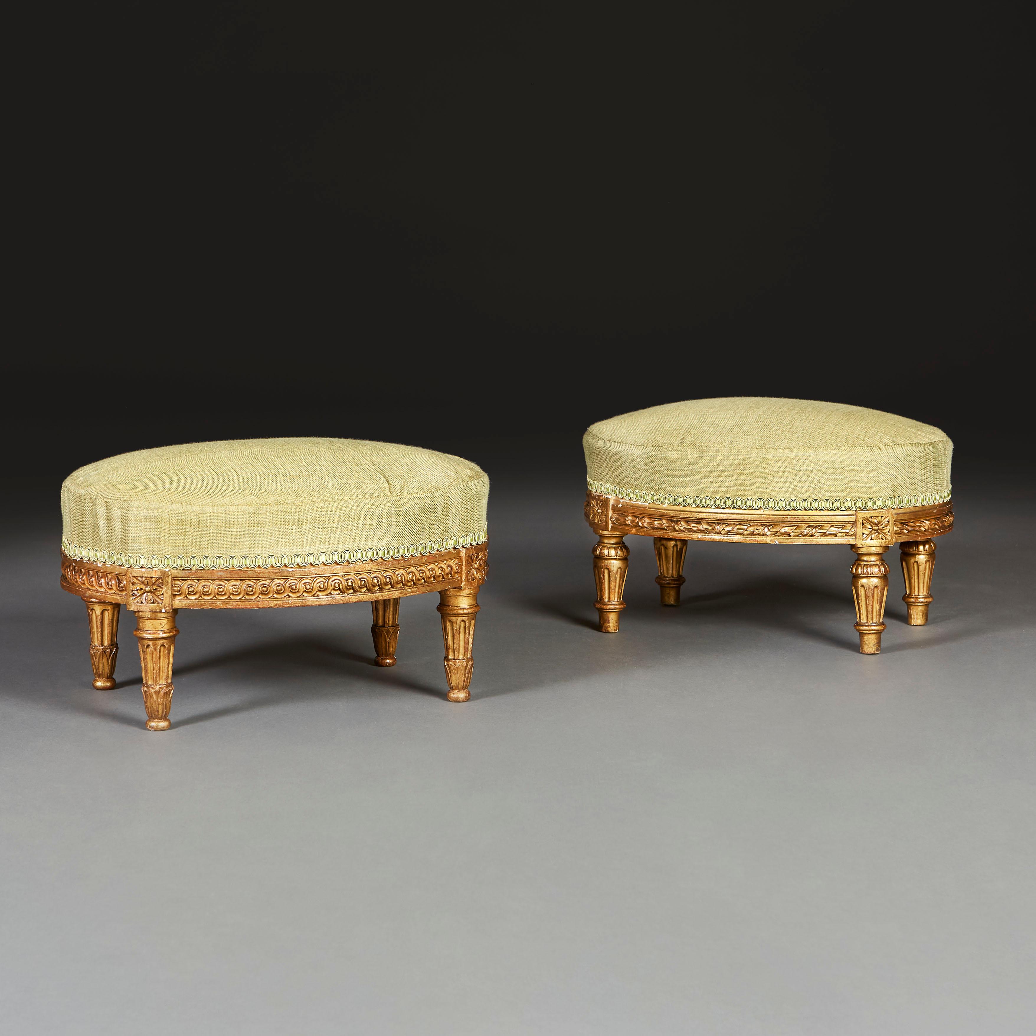 Paire de poufs en bois doré du XVIIIe siècle, de forme ovale, avec un décor guilloché sculpté sur la barre d'assise, entrecoupé de paterae au-dessus de quatre pieds godronnés et effilés. Aujourd'hui, il est recouvert de soie verte. Avec les marques