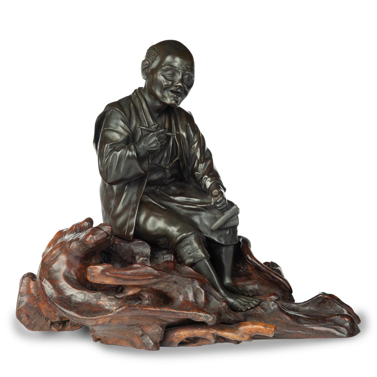 Bronze aus der Meiji-Periode eines sitzenden, rauchenden Mannes, der seine Pfeife in der rechten Hand hält und auf einem Wurzelholzsockel ruht, in Handwerkerkleidung und mit nackten Füßen, das Gesicht ausdrucksvoll geschnitzt,  unterzeichnet mit dem