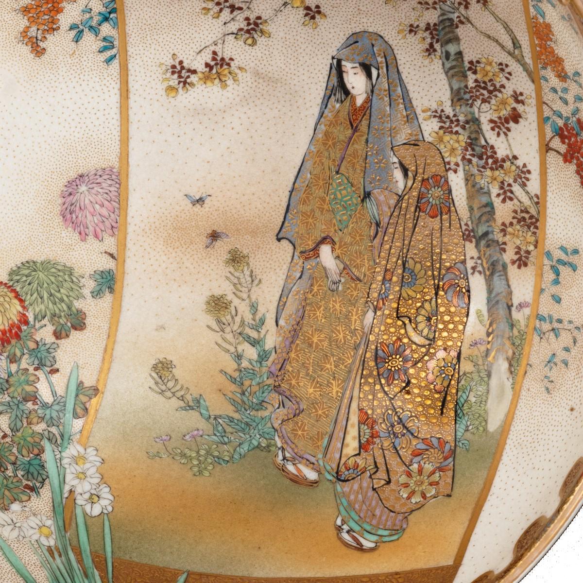 A Meiji period Satsuma earthenware bowl, painted in coloured enamels and over-glaze gilding with two ladies wearing brocade robes in a framed panel against flowering plants on a gold-stippled ground, the exterior with a continuous comb-tooth