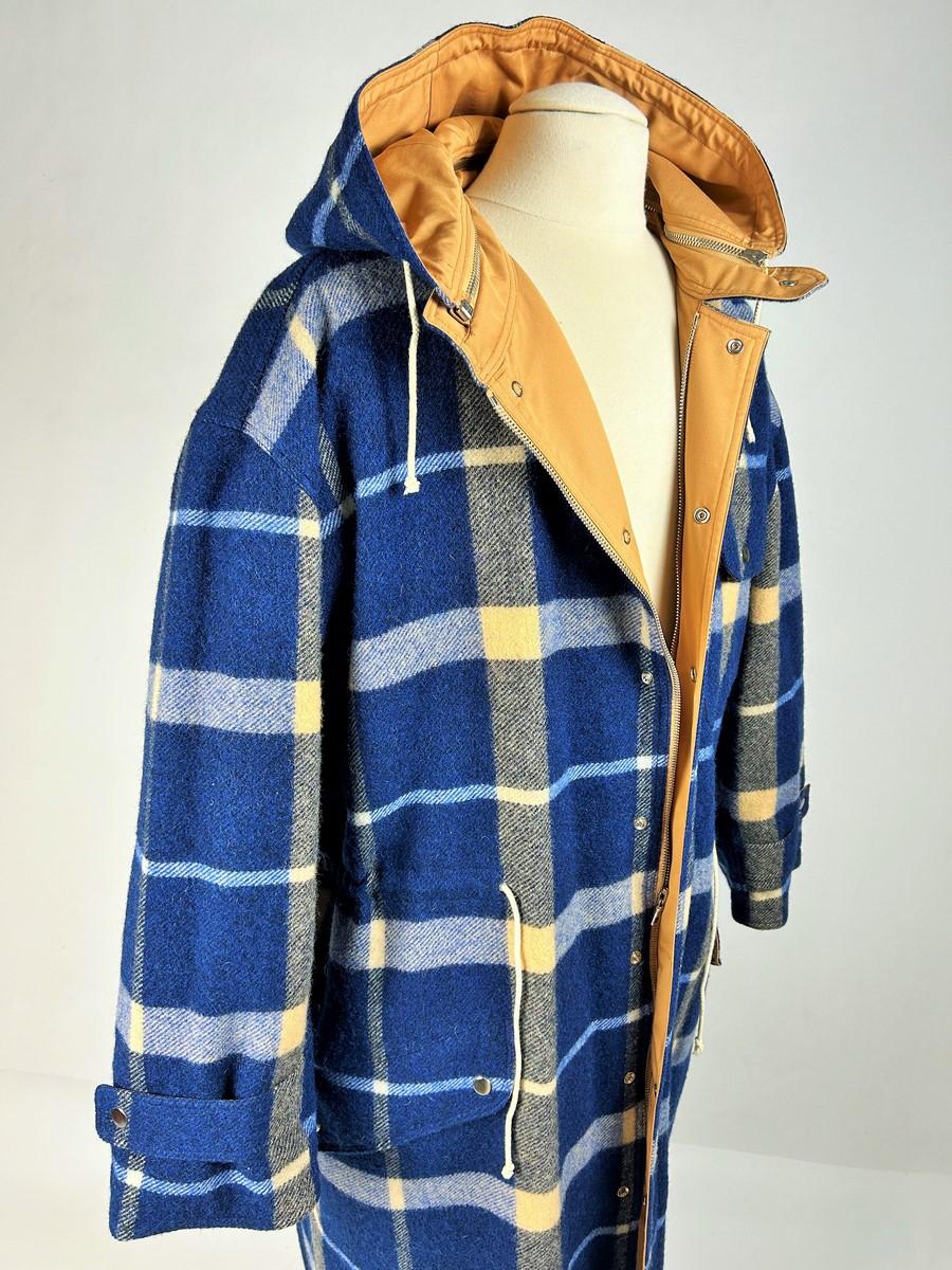 Circa 2000

France

A large Men's Trenchcoat in wool tartan check in mint condition dating from 2000. Long coat with zip and press studs and removable hood. Three flap pockets with press studs and reminder on the cuffs. Navy blue tartan with large