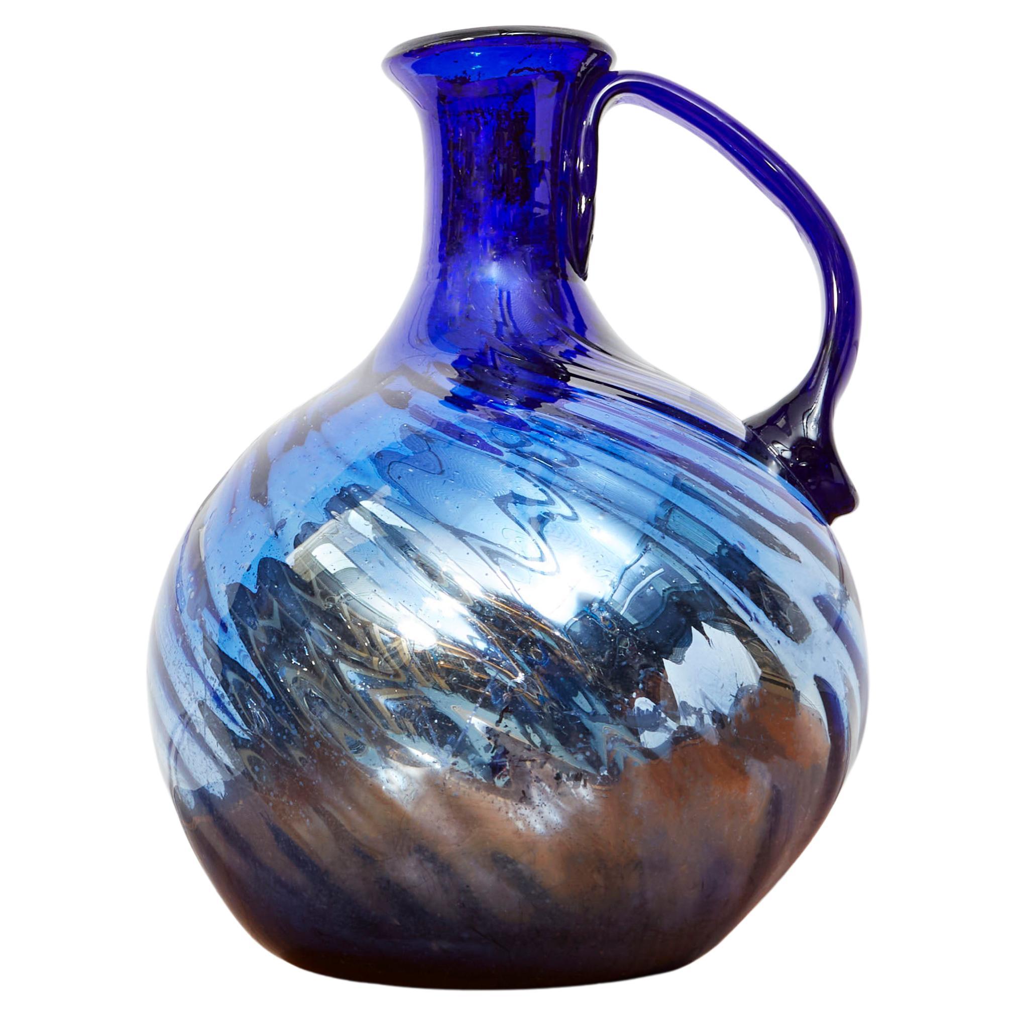A spectacular wrythen moulded blue and mercury glass jug with spherical body, tapered neck and with single loop handle.

Continental, Early Twentieth Century.