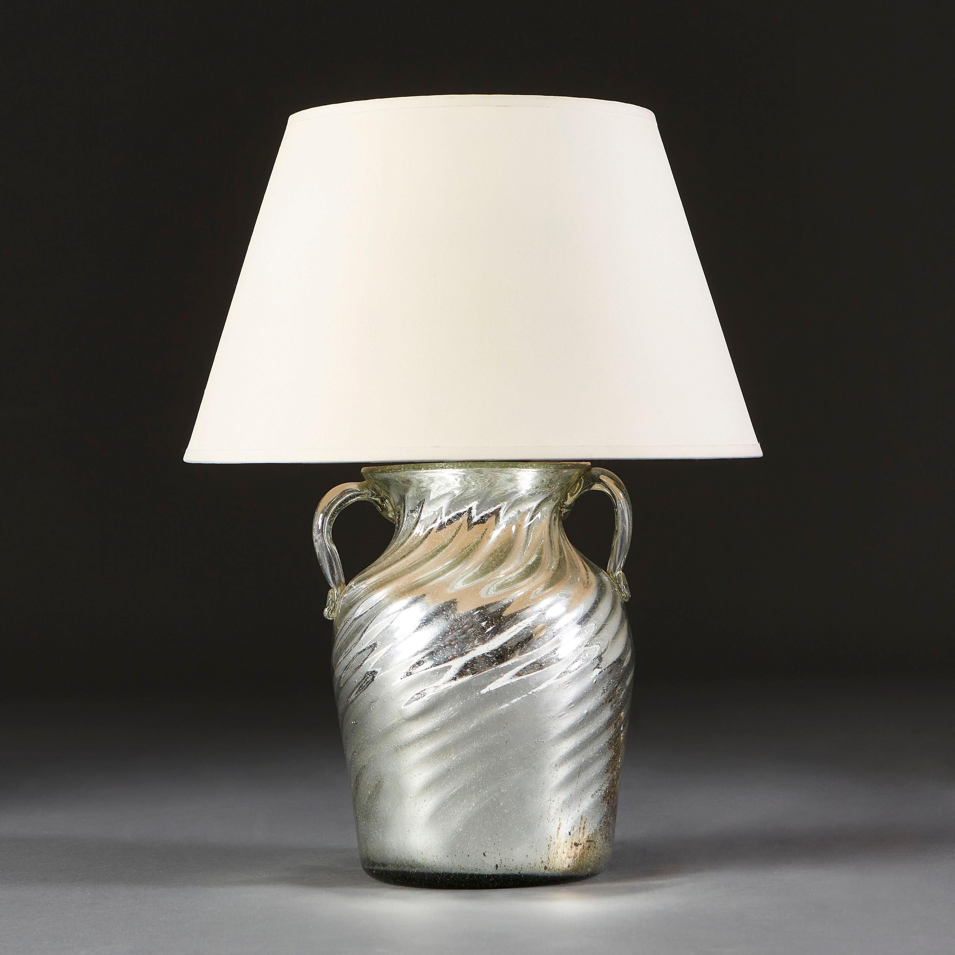 A mercury glass vessel, with a twisted body and flared neck, decorated with two handles, now as a lamp.

Currently wired for the UK. 

Please note: Lampshade not included.