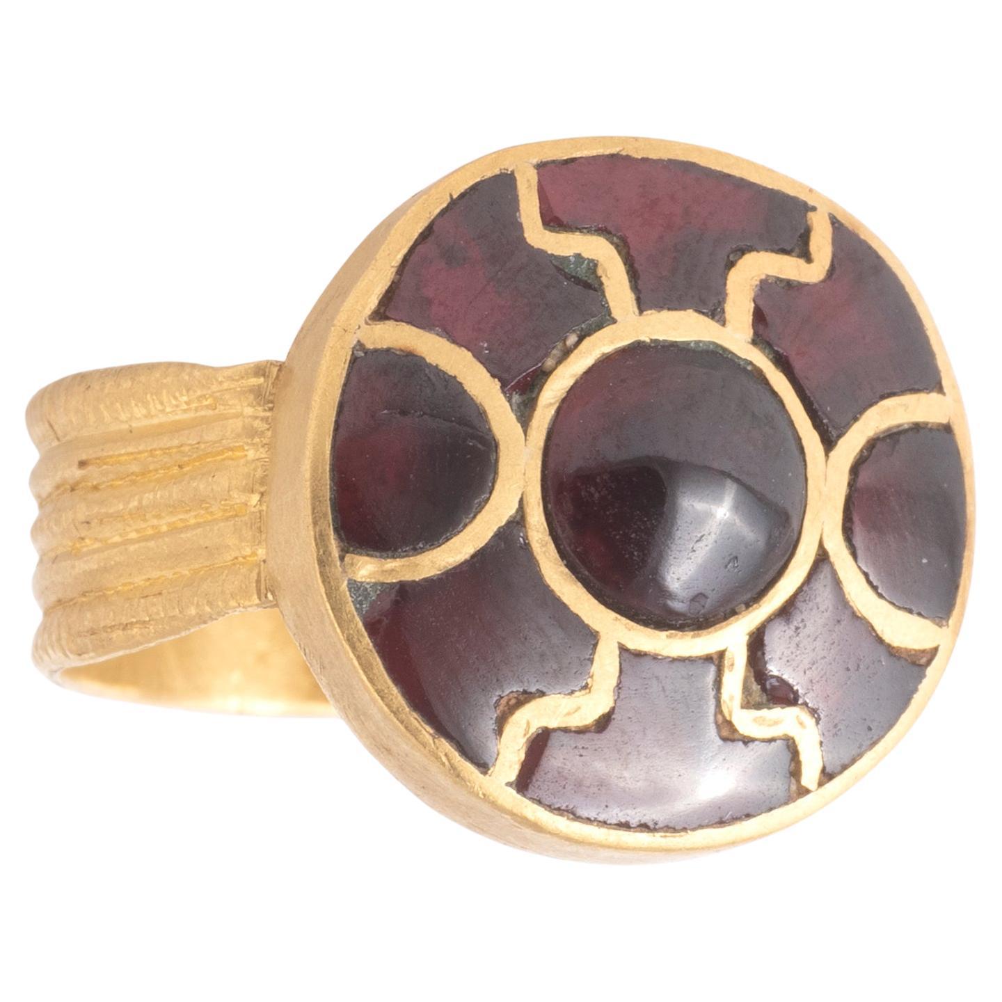 The hoop formed of two wire ropes, joined to the underside of the circular two-stepped bezel by sheet strap and twisted wires, the outer edge grooved, the bezel with nine cloisonnés set with foil-backed garnets in a rosette pattern
Top size: