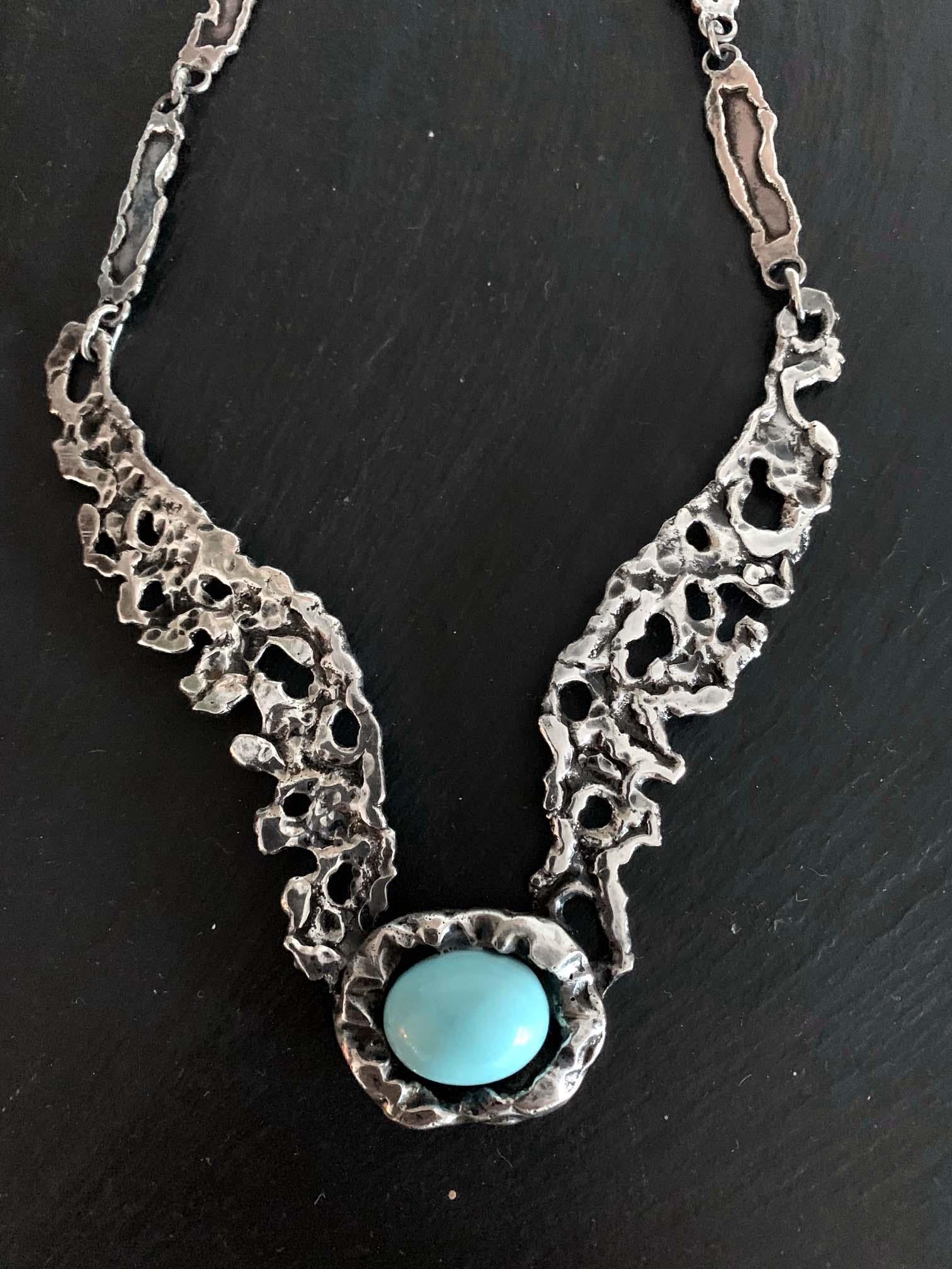 A sterling silver necklace with a turquoise color cabochon set in by Mexican silversmith Tane Orfebres circa 1960-1970s. The chain links were crafted in a modernist sculptural form with an aesthetic of brutalism. The lower bands were fixed with the