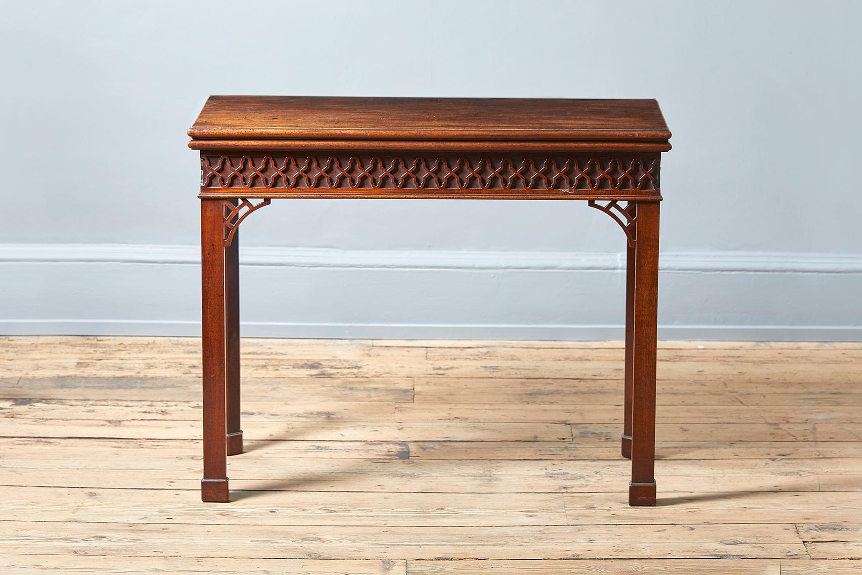 A George III mahogany folding card table, circa 1760, the moulded top opening to a baize lined interior, the blind fretwork decorated frieze above square section legs surmounted by pierced brackets and on plinth feet, hinges stamped H Tibats.

The