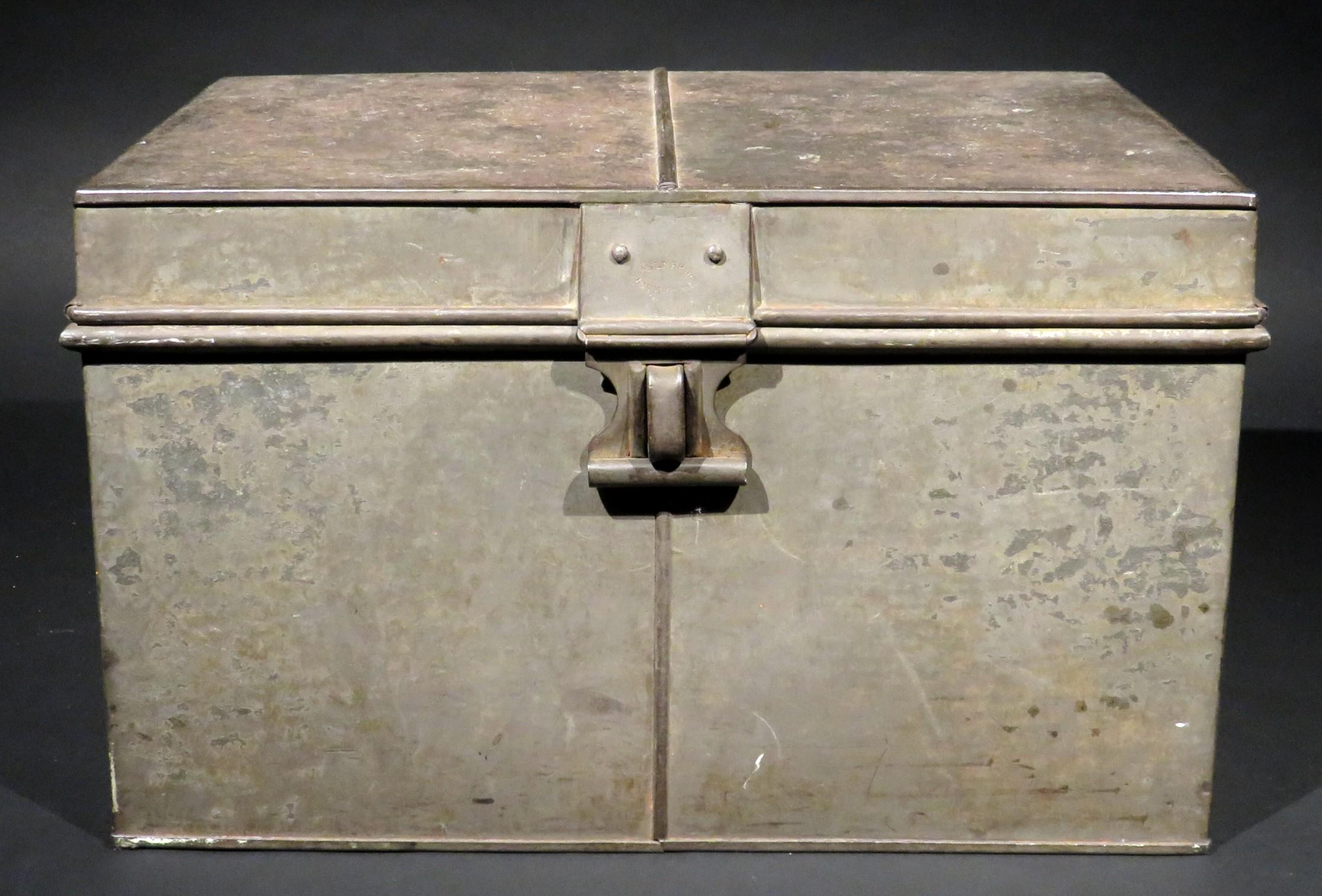 Eine originale Thomas Milner Sicherheitsbox aus Eisenblech mit gelöteten Nähten, ausgestattet mit zwei aufklappbaren Tragegriffen und einem aufklappbaren Deckel. Der Verschluss des Deckels trägt gestempelte Herstellermarken, die Unterseite des
