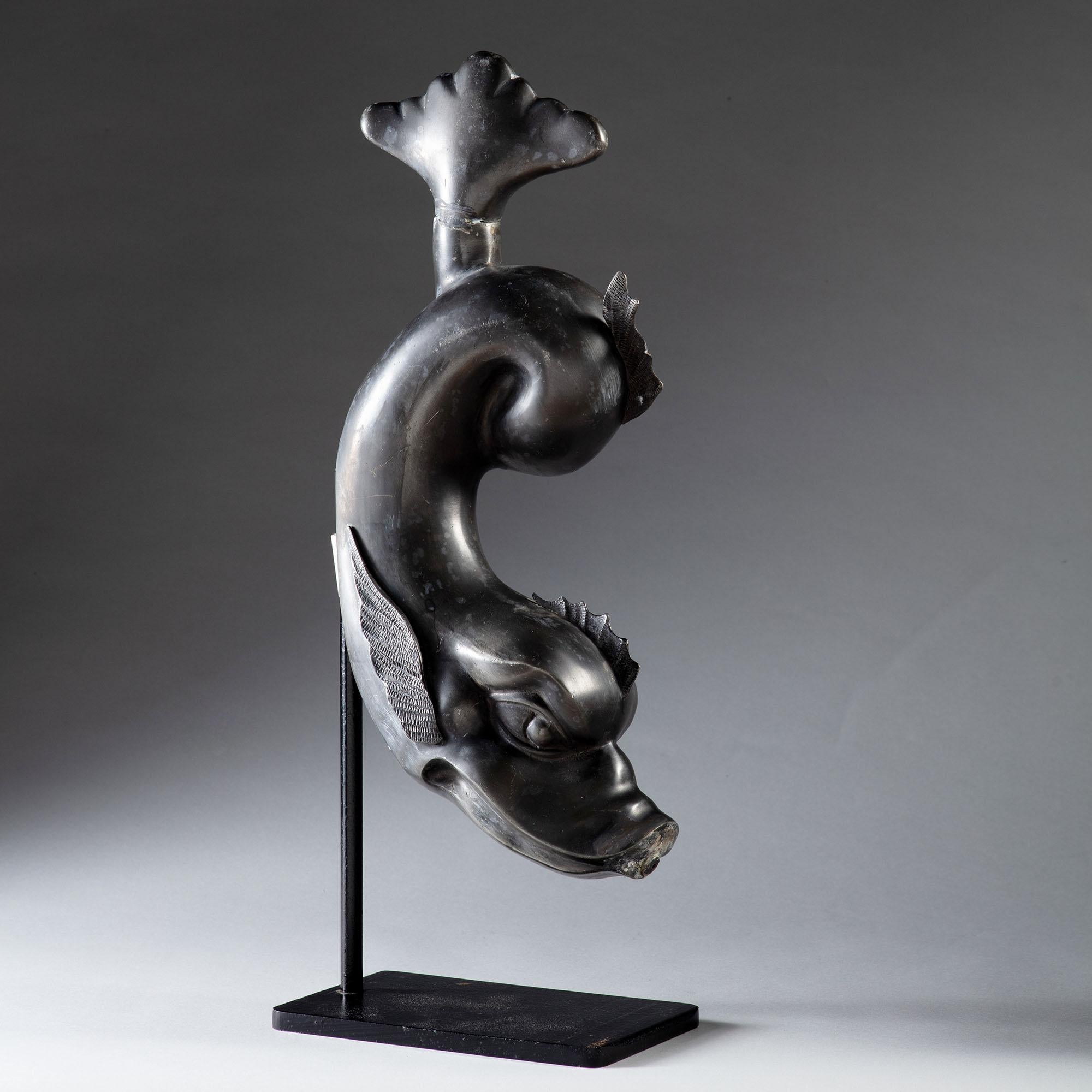 A mid-19th century lead dolphin spout, with twisted tail and finely detailed fins, now mounted on a cast iron stand.