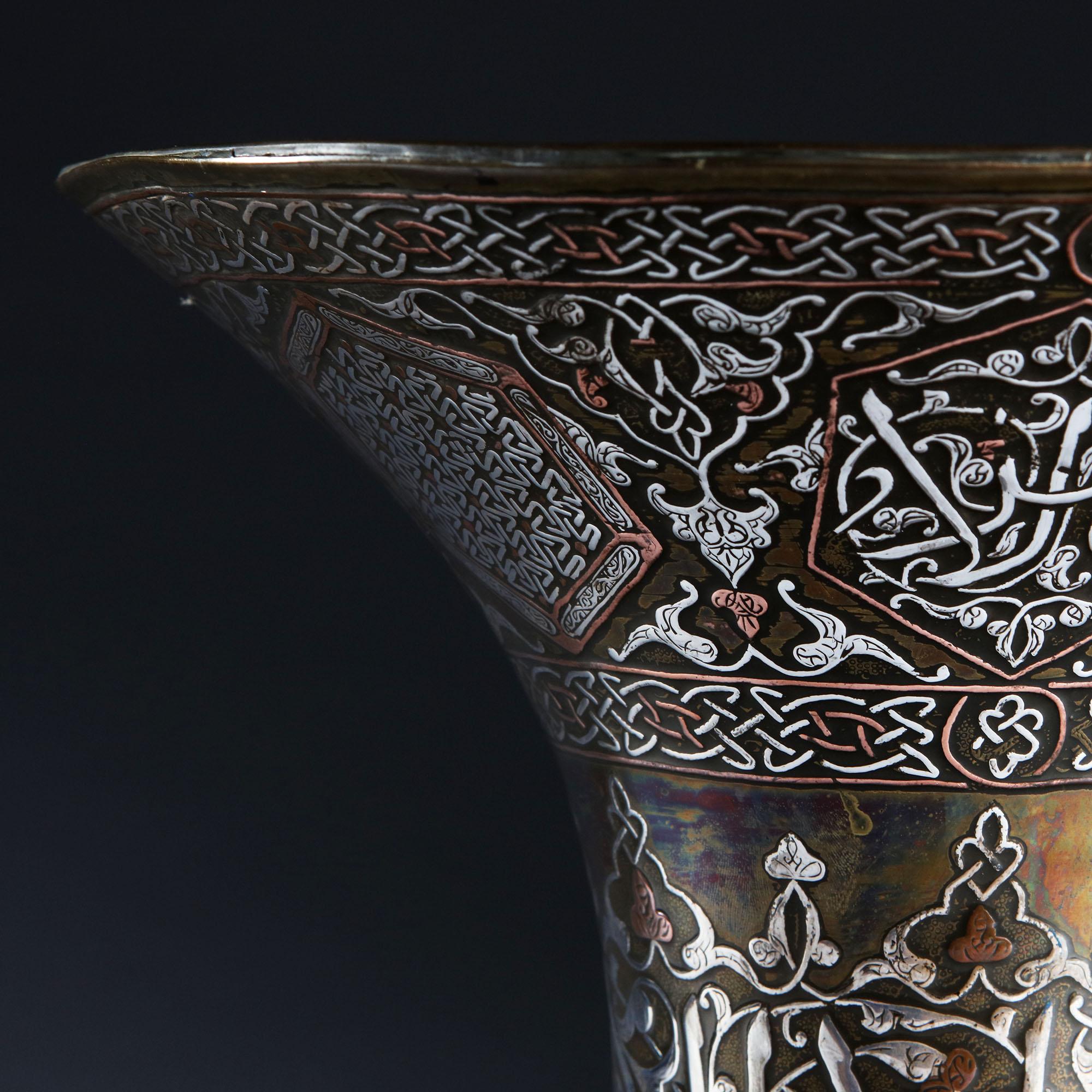 A 19th century Ottoman trumpet vase in silver, copper and brass, with flared neck and with Islamic script and pattern inlay throughout.