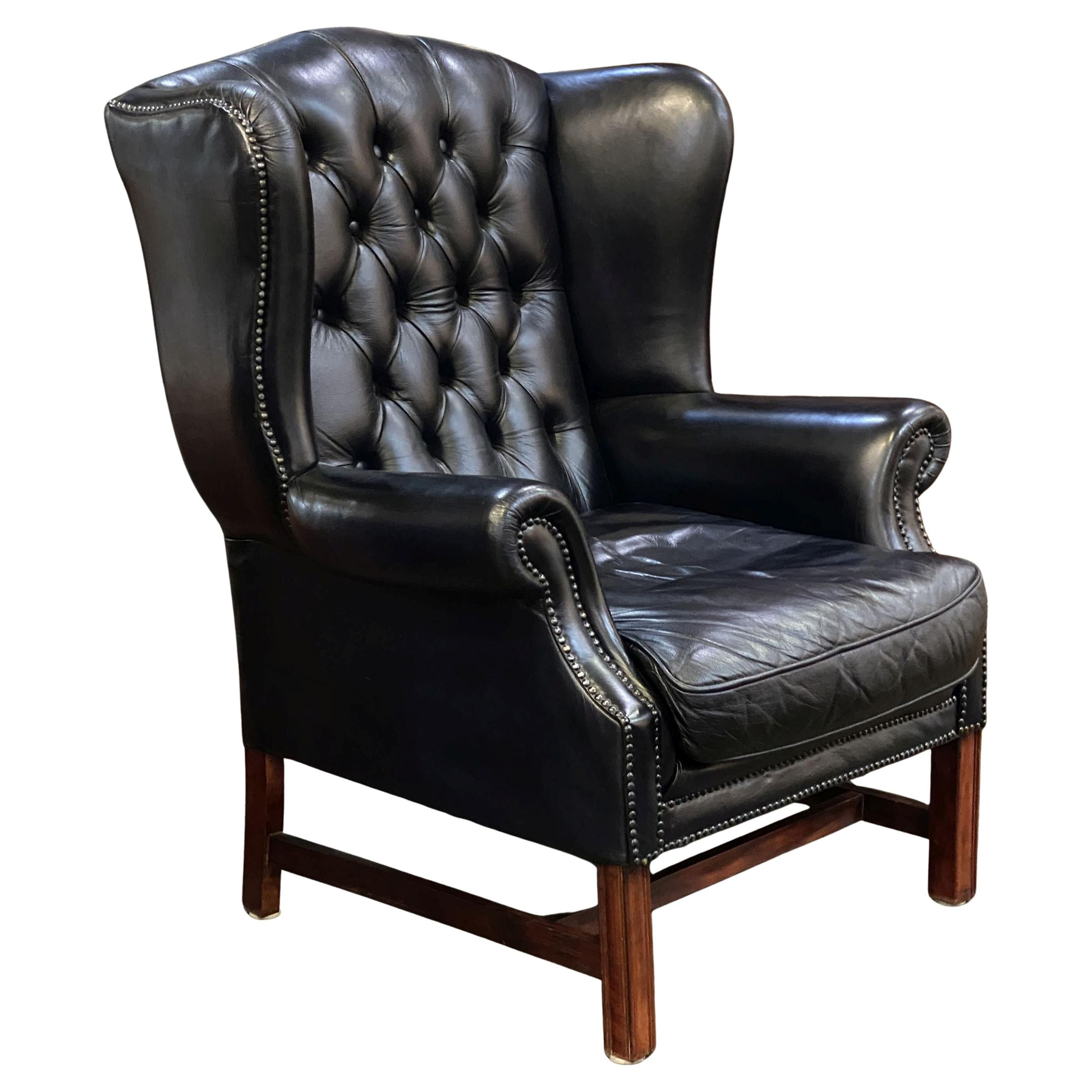 A fine English wingback armchair or lounge chair upholstered in black leather and patinated mahogany in the George III style  - featuring a high back, winged sides and shaped arms, with a large comfortable seat and drop-in cushion, resting on a