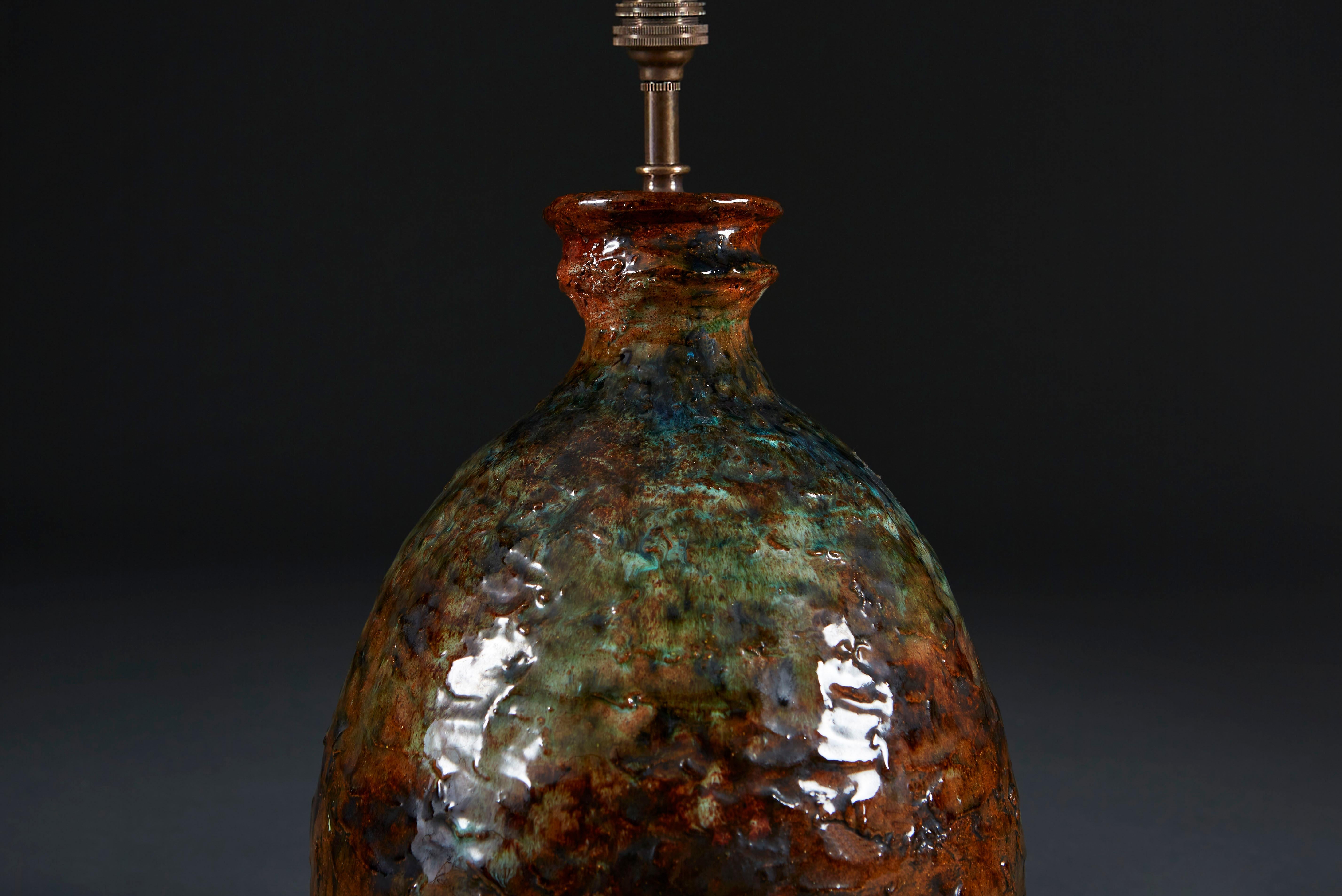 A mid-20th century art pottery vase with an unusual volcanic glaze of rust and green pigments, now converted as a lamp.

Please note: lampshade not included.

Currently wired for the UK.