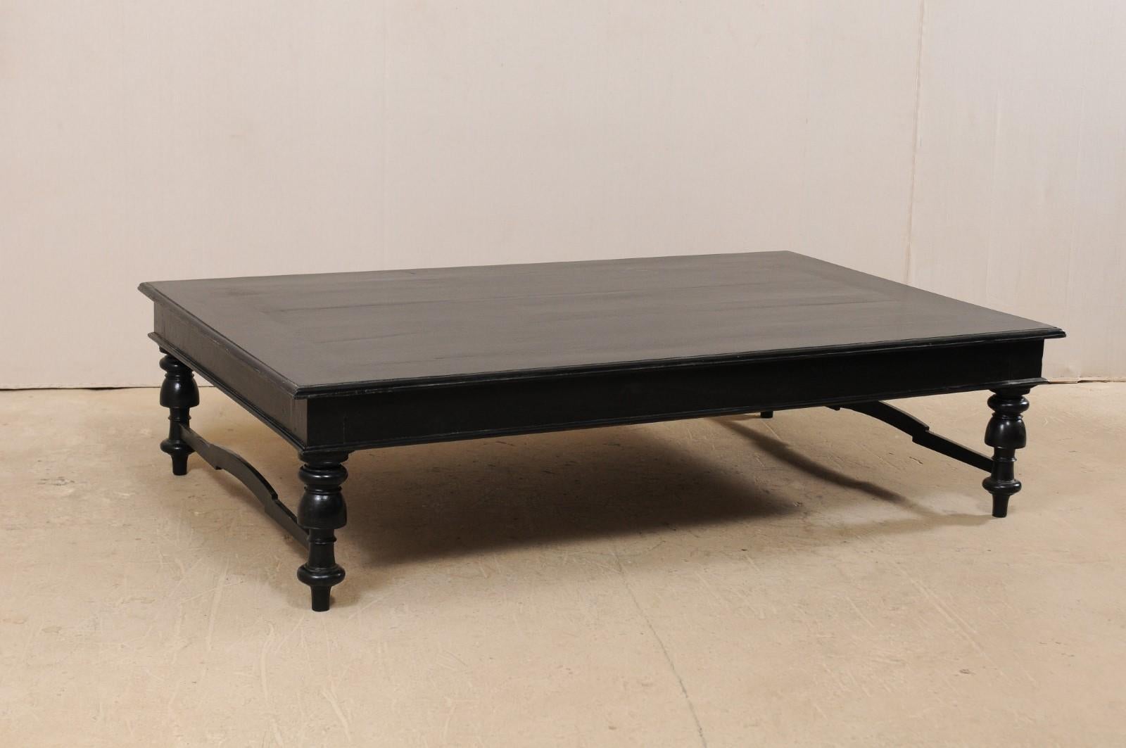 A handsome black British Colonial day bed, from the mid-20th century, which makes for a wonderful modern-use coffee table. This vintage piece from India features a 7 ft long, rectangular-shaped top with thick apron, which rests upon four beautifully