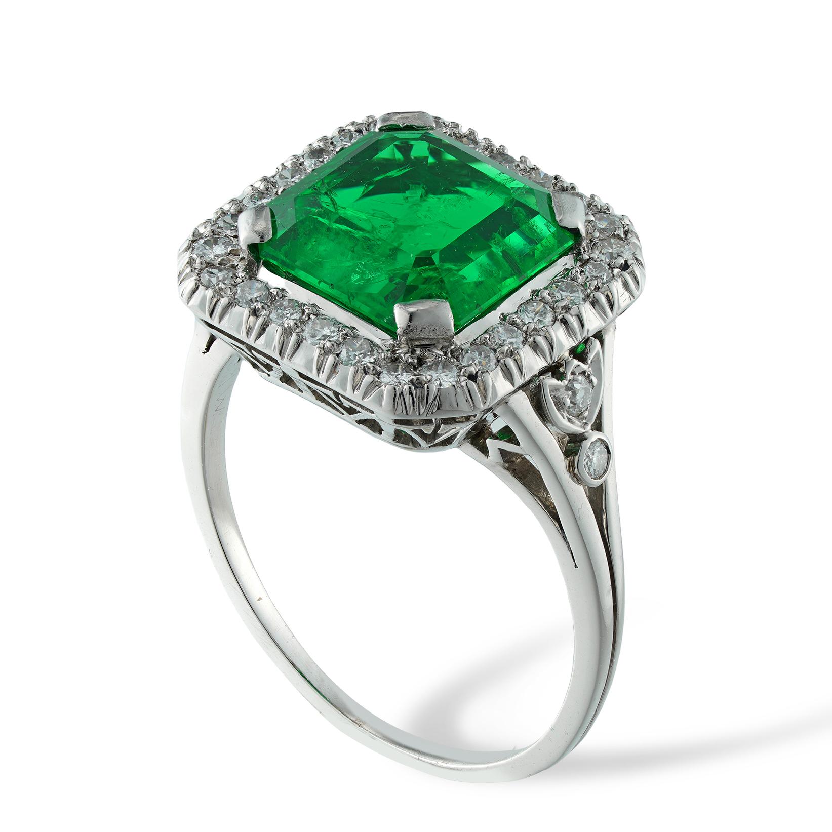 A mid-20th century emerald and diamond cluster ring, the octagonal-cut emerald weighing 2.84 carats, accompanied by GCS Report stating to be of Colombian origin, four claw-set surrounded an octagonal frame set with twenty-six round brilliant-cut