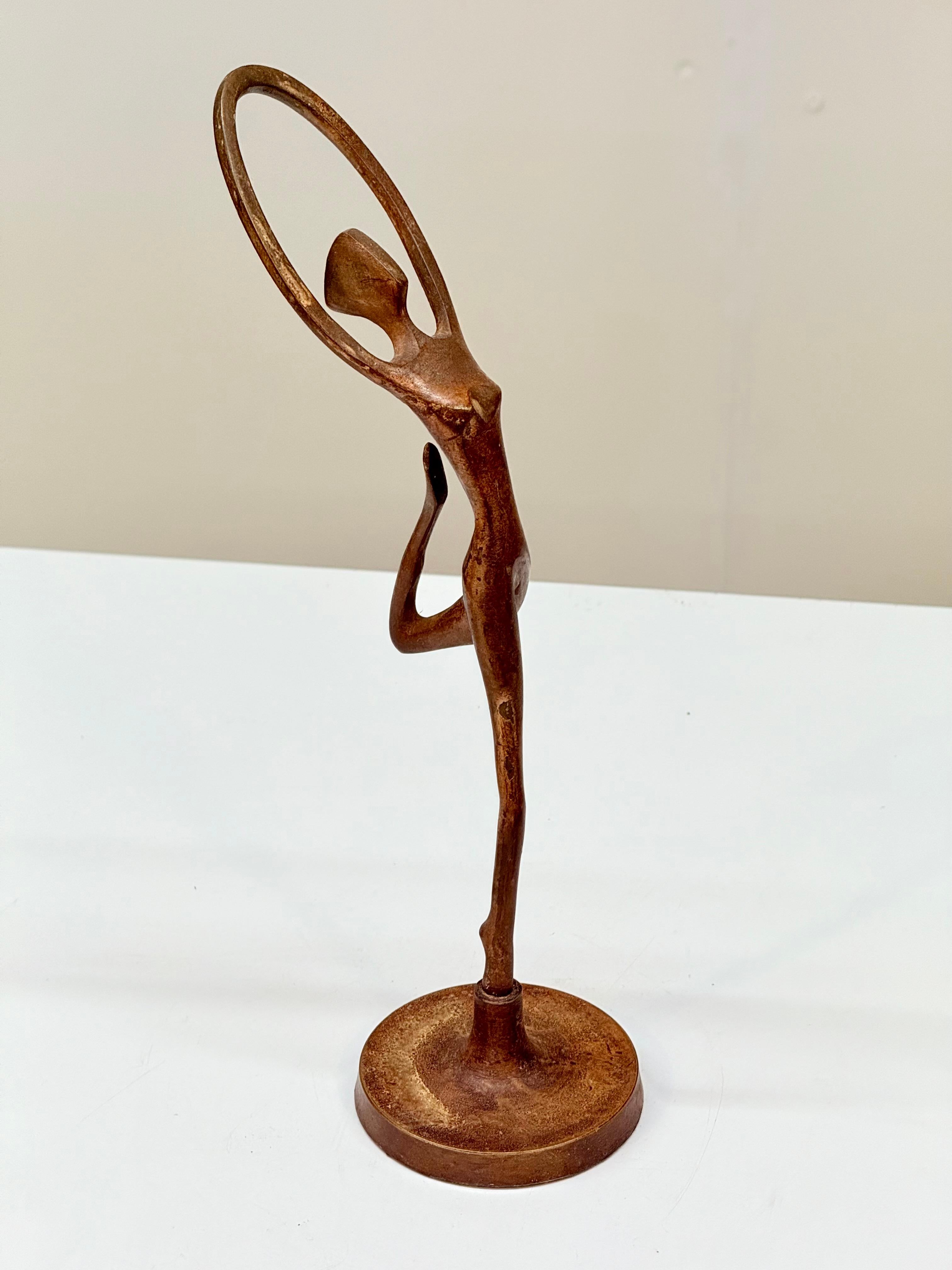 Una statuetta in bronzo francese della metà del XX secolo raffigurante una ballerina stilizzata in una posa fluida, con le braccia che formano una forma circolare sopra la testa e un ginocchio piegato, che cattura la bellezza del movimento. La forma