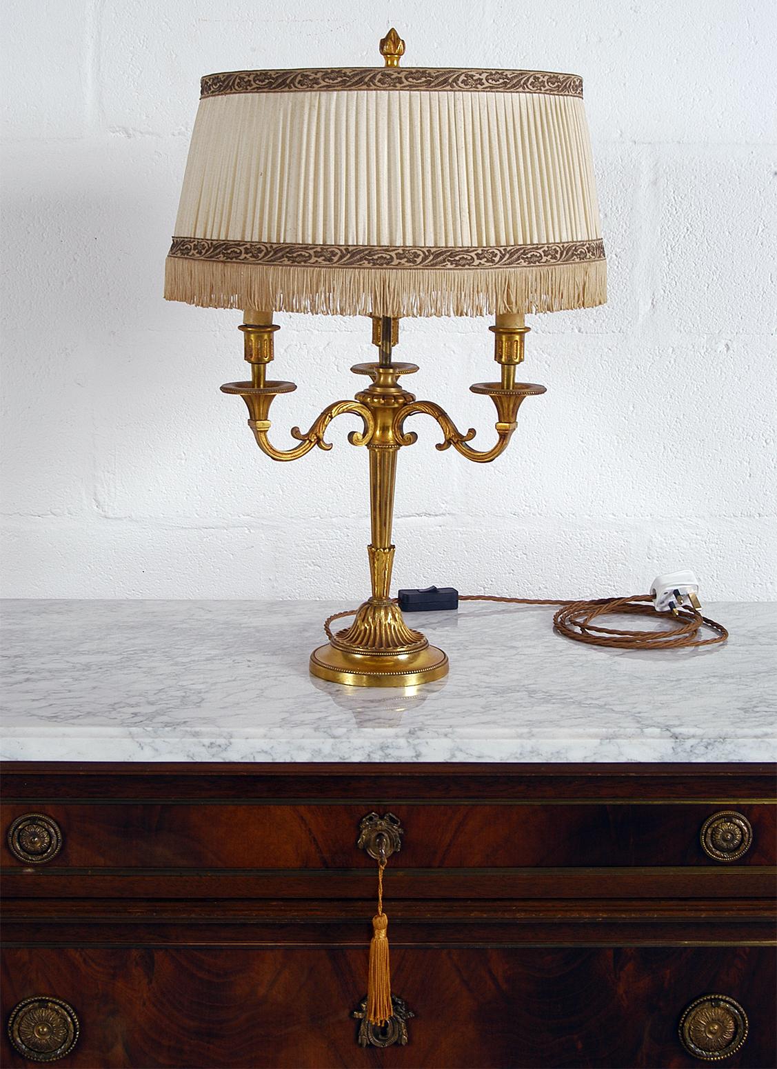 This attractive mid-20th century French gilt brass Bouillotte three-arm table lamp has a heavy brass base and retains its original pressed card faux candles and fringed pleated shade.
It has been gently cleaned and rewired to UK 240v specification,