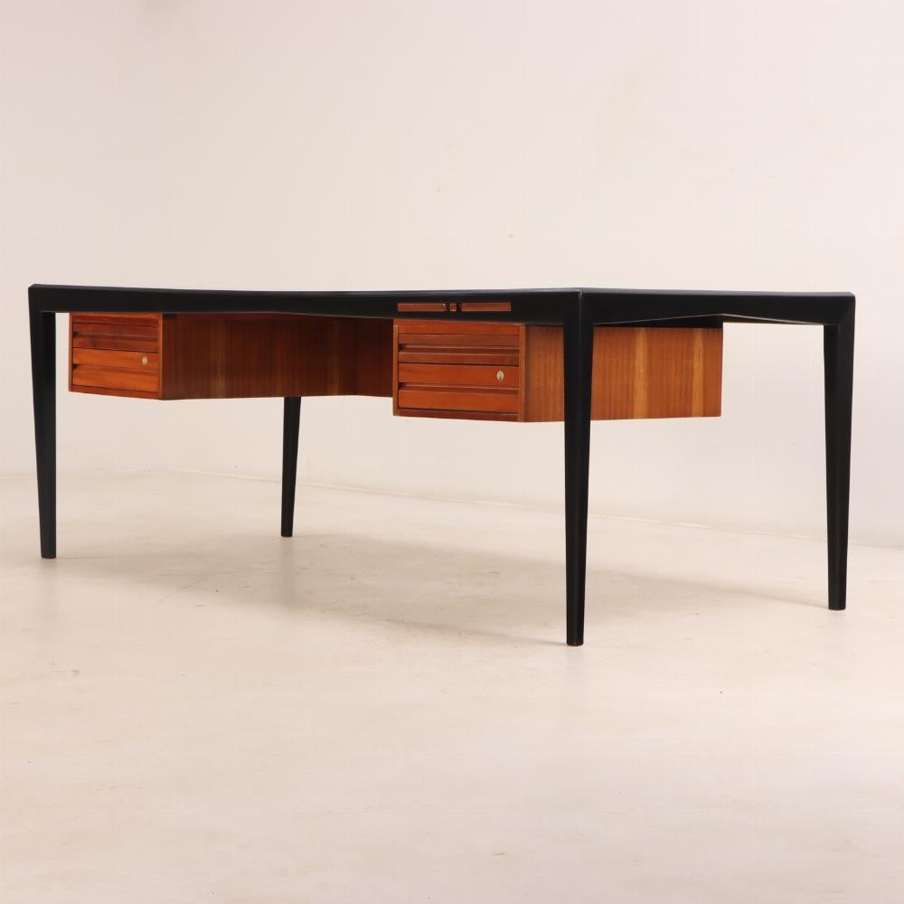 Questa scrivania moderna del Mid-Century in mogano e mogano ebanizzato ha un design minimale ed elegante. Il piano e i piedistalli in mogano sono sostenuti da una struttura in legno ebanizzato. Con 5 cassetti e un look elegante, questa scrivania è