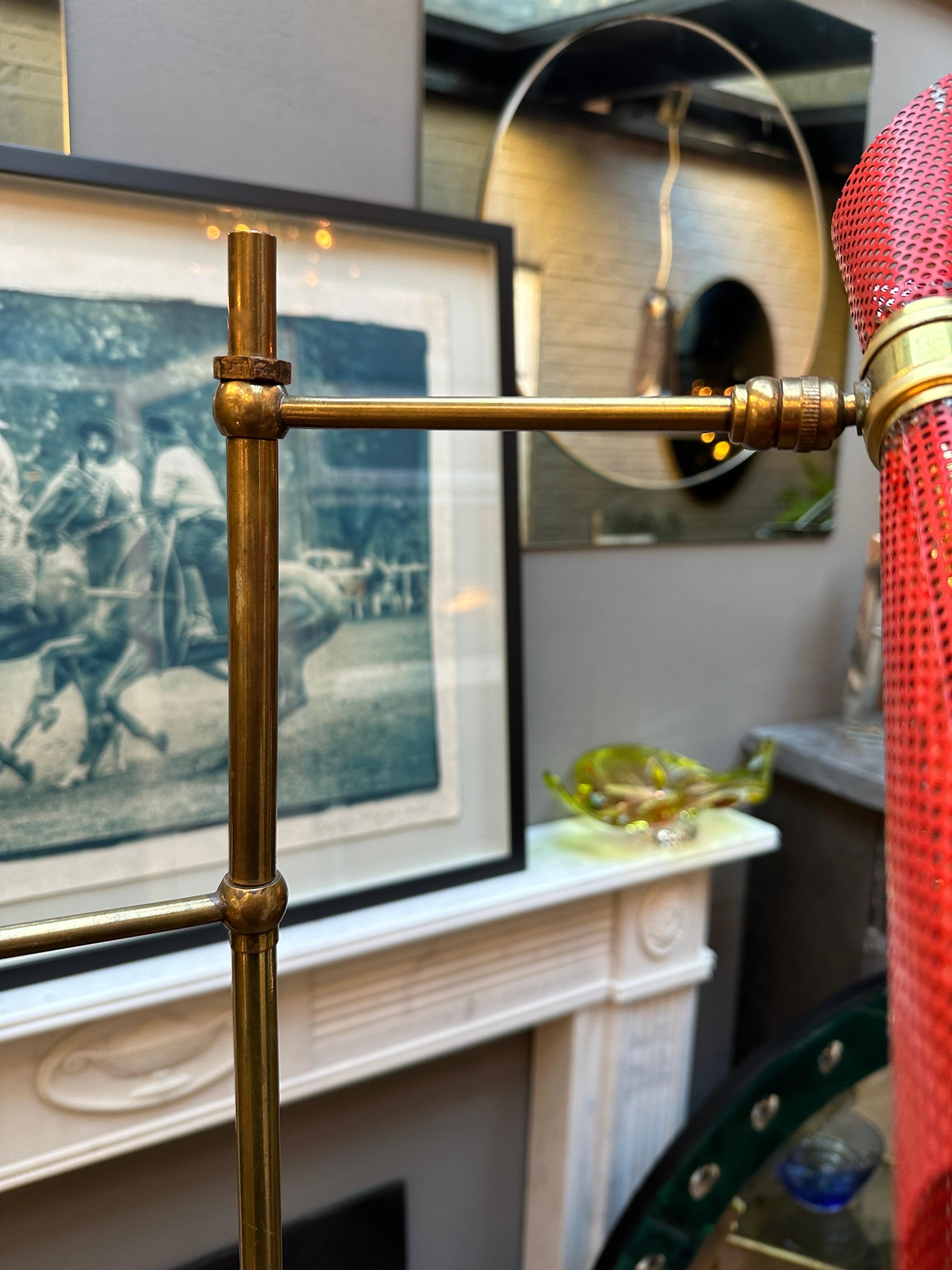 A French twin arm with tripod foot brass floor lamp. The adjustable and pivotable heads in red and yellow, the top arm able to move round the stem to give different lighting. The shades perforated. The stem and tripod foot in slender simply designed