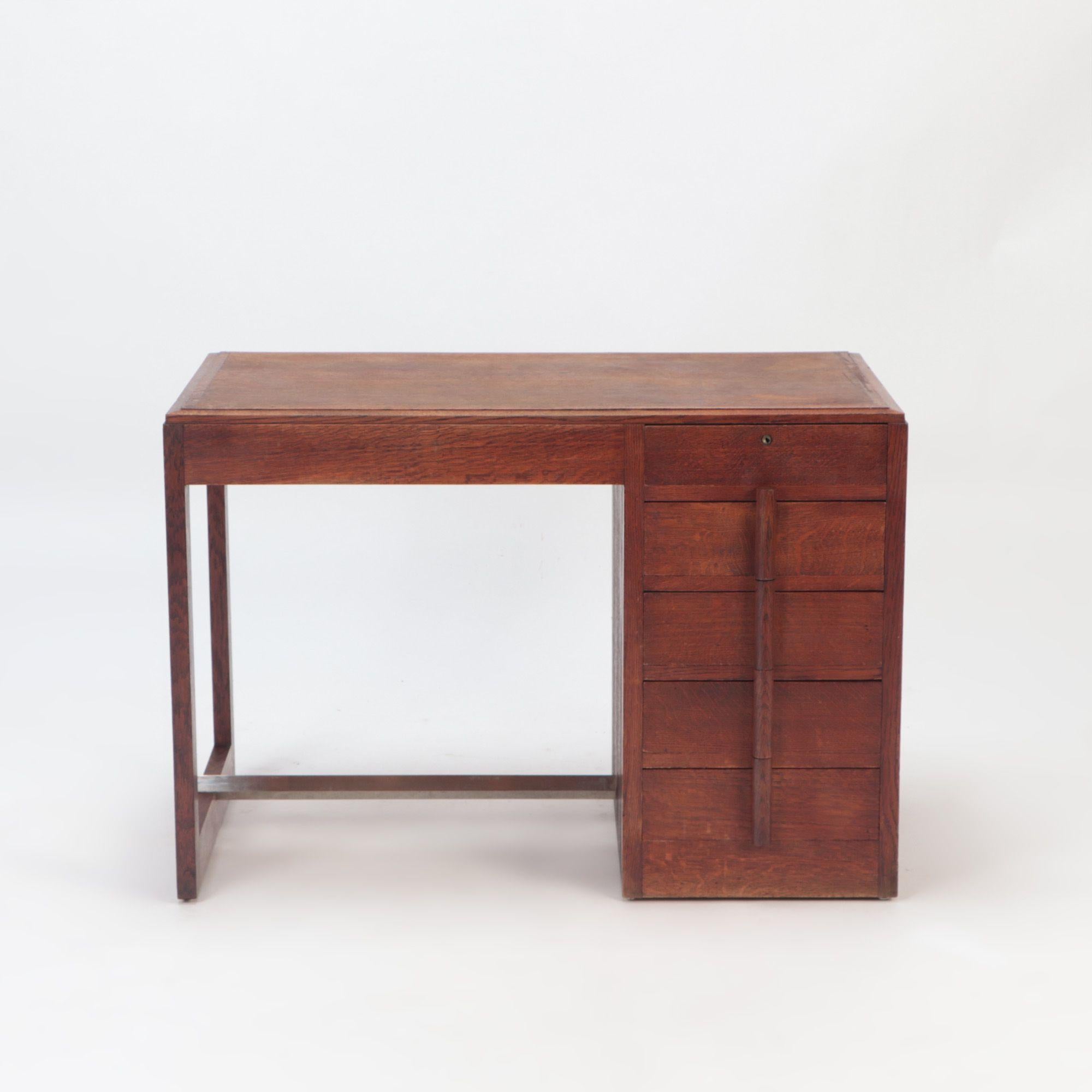 A French oak desk in the manner of Charles Dudouyt. The desk features 5 front drawers and a metal stretcher at the base. Circa 1940.