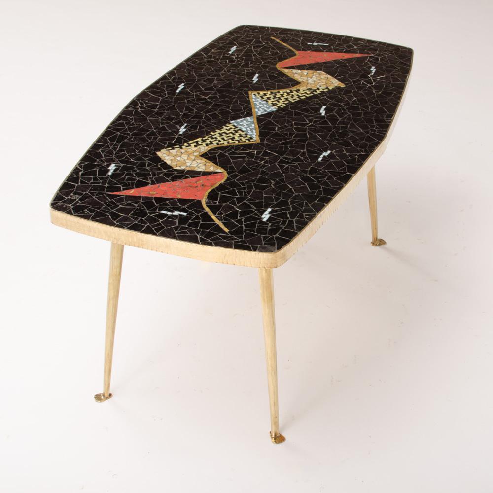 Une table en mosaïque allemande du milieu du siècle avec des carreaux de mosaïque multicolores. La table a une forme intéressante de double trapèze. Le bord du plateau de table est en métal, tout comme les pieds de table effilés. Le dessus contient
