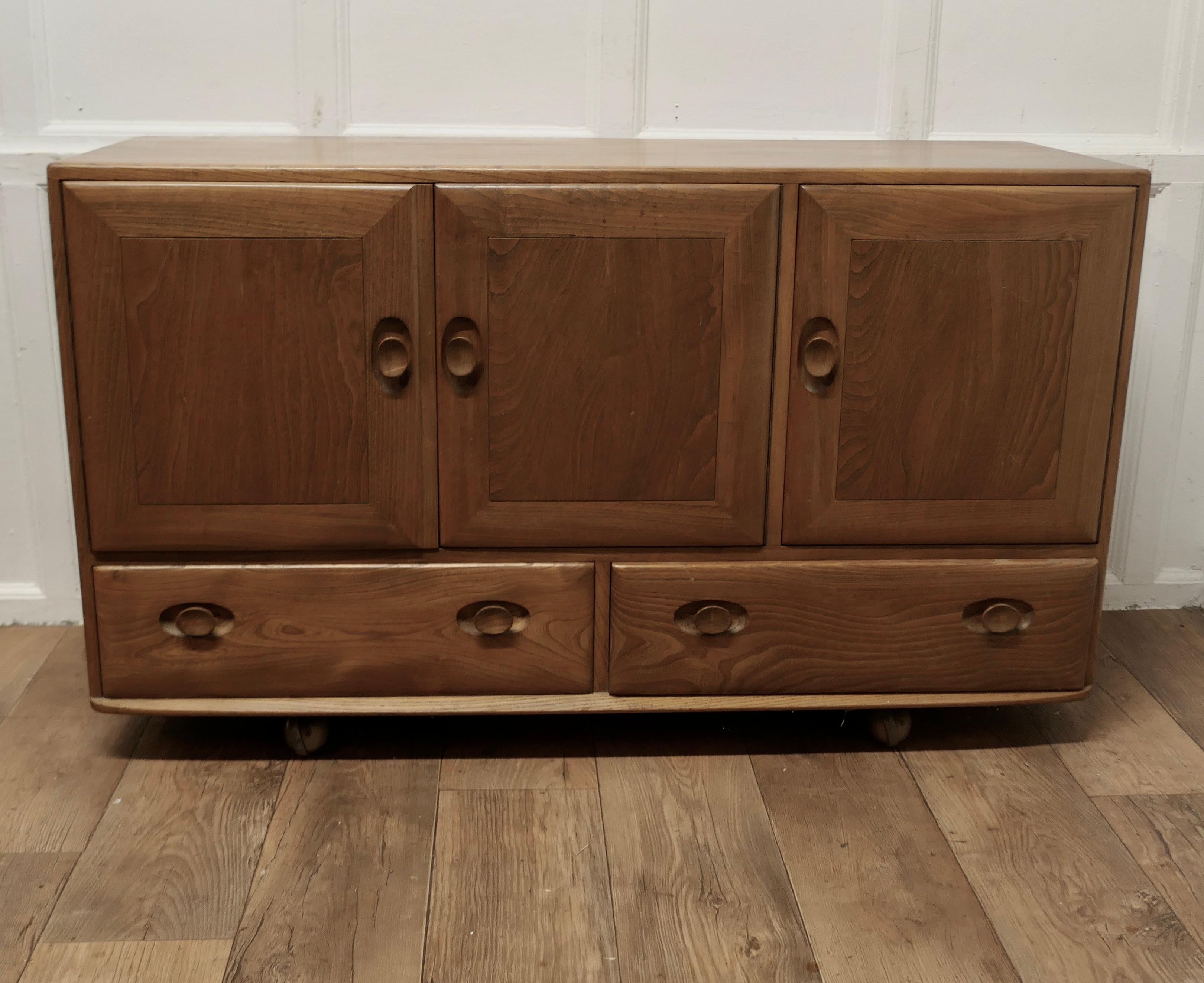 A Mid Century Golden Elm Sideboard by Ercol

The sideboard has 3 cupboard doors and 2 long drawers below, it has inset turned handles and it stands its original ball castors 

The sideboard has an elm top and it has a cutlery tray in the end