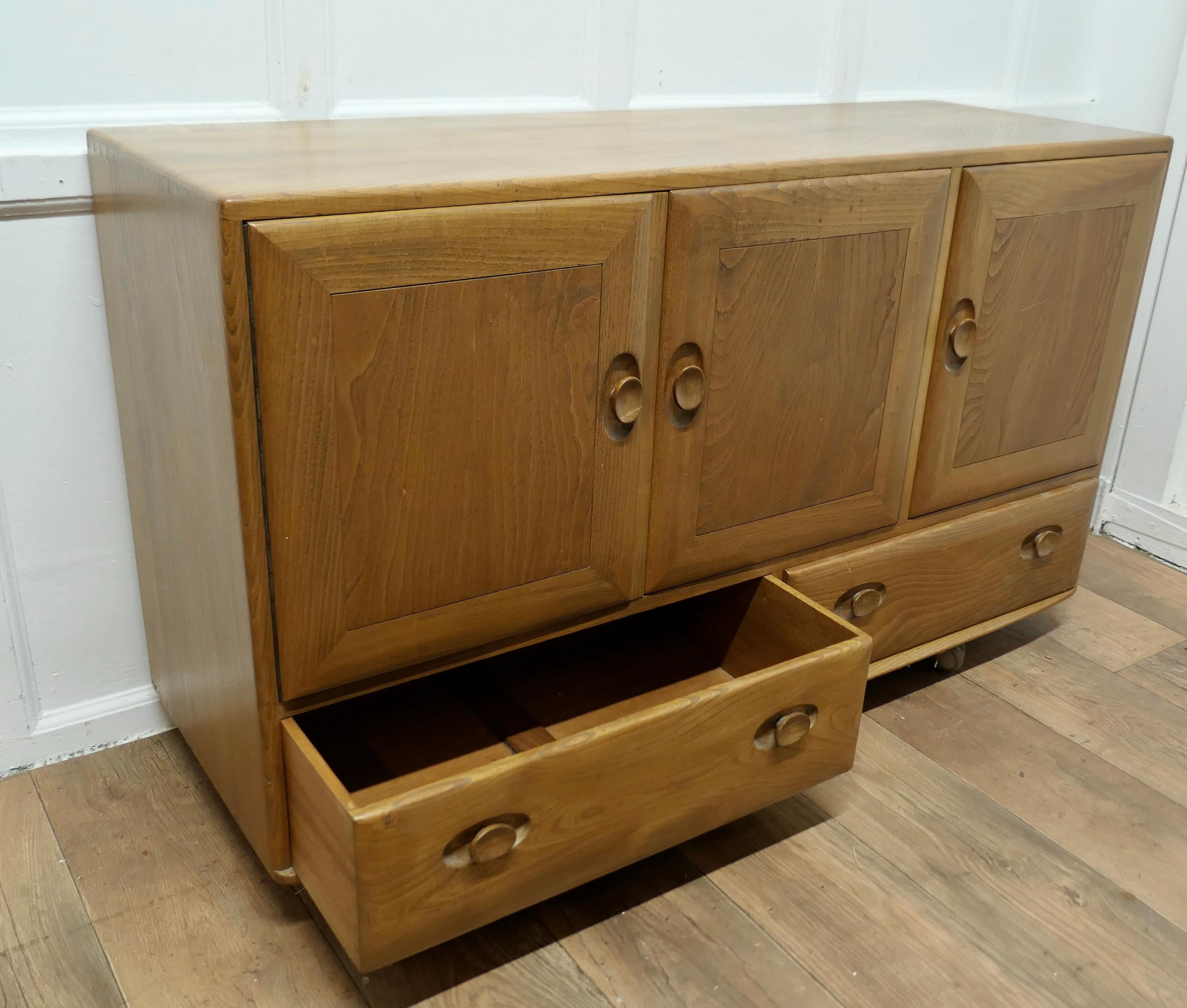 A Mid Century Golden Elm Sideboard by Ercol  The sideboard has 3 cupboard doors  2