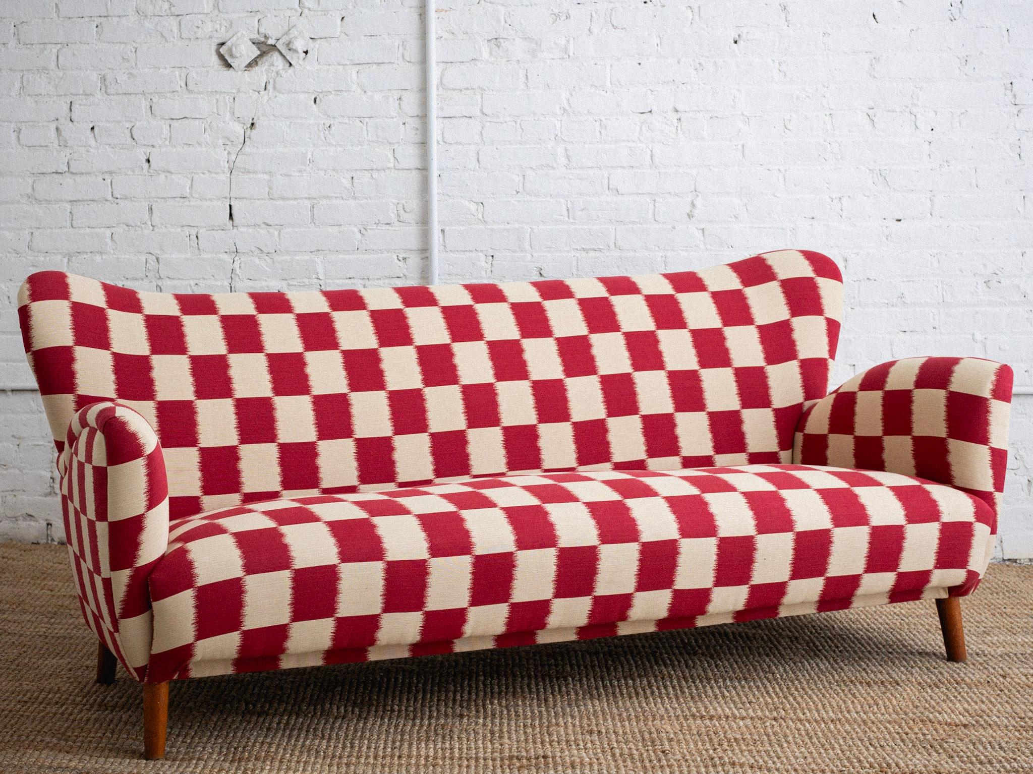 A mid century Italian sofa. Low profile and wingback style silhouette. Newly reupholstered in a red and cream ikat checkered jacquard. Sourced outside of Florence, Italy. Matching side chair also available, sold separately.