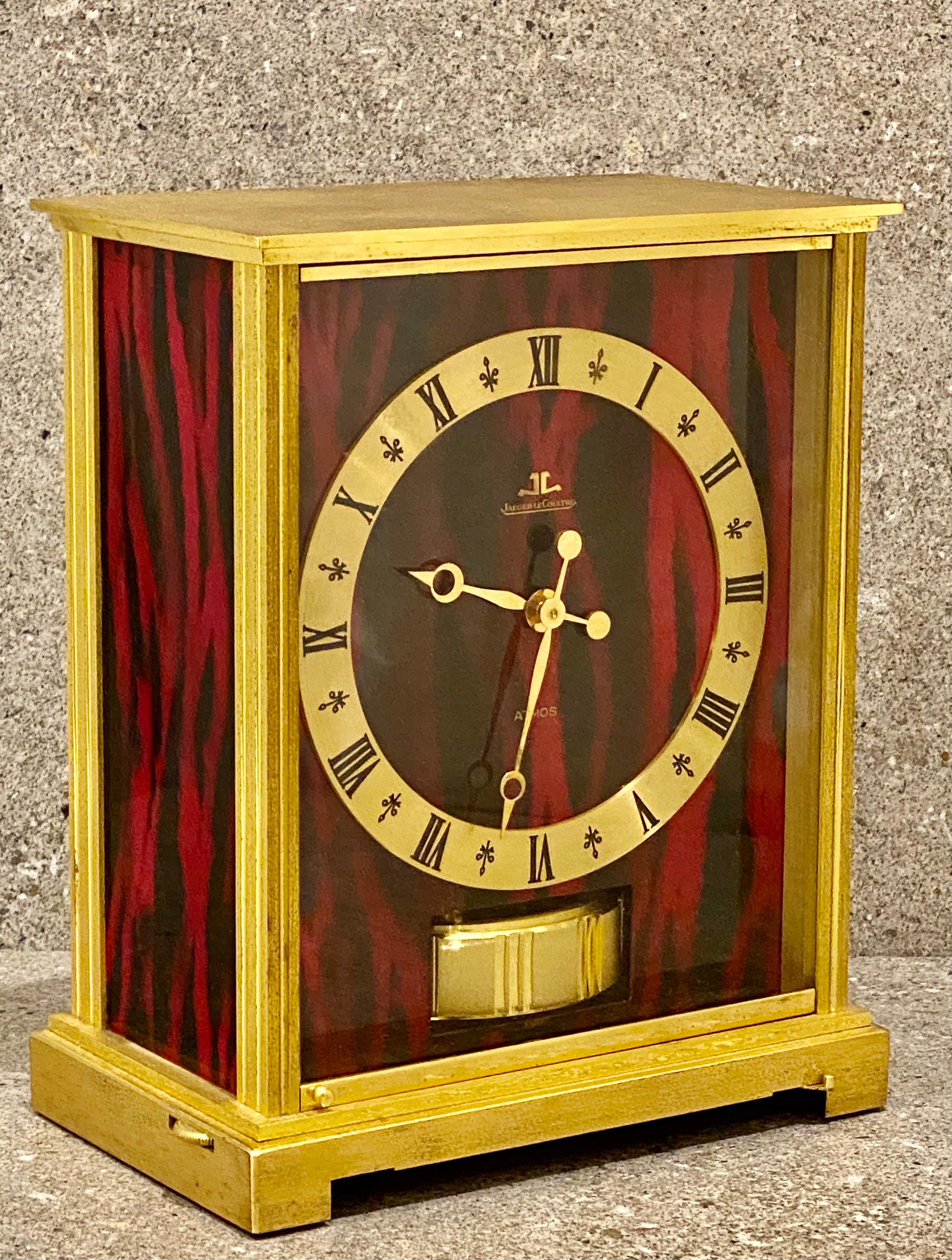 A nice example of A Jaeger-LeCoultre Atmos clock, Embassy, signed Jaeger Le Coultre, with red and black faux marble panels, base with stop lever, dial with Roman chapter ring and visible balance wheel below, 22cm high, with Jaeger Le Coultre booklet