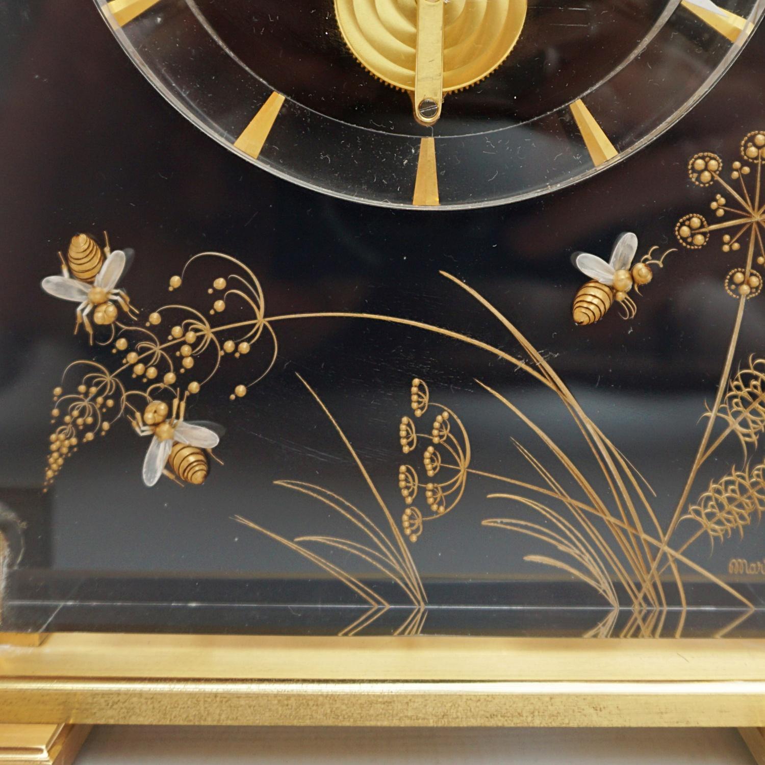 A Mid-Century Jaeger-LeCoultre mantel clock in a Lucite case with inset brass decoration showing Bumble Bees amongst various flowers and branches . Set over a gilded Brass stepped base. Eight day movement by Jaeger-LeCoultre with baton numerals and