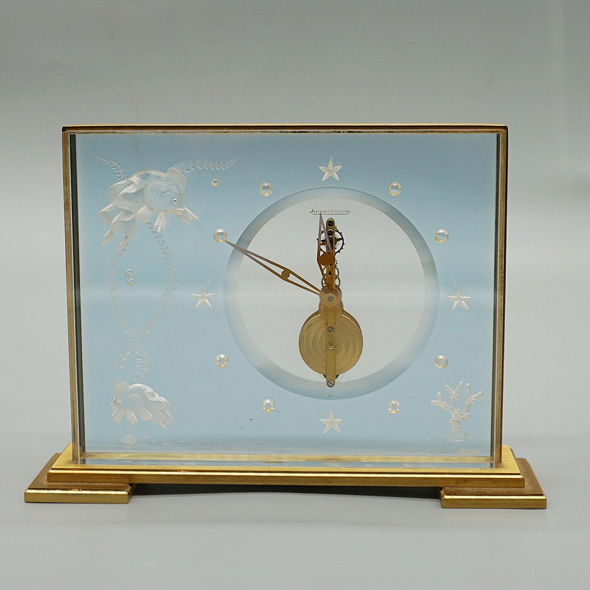 A mid-century 'Marina' mantel clock by Jaeger LeCoultre. Lucite case with inset decoration featuring fish amongst coral with water drop numerals and original gilded hands. Set over a gilded brass stepped base. Eight day movement by Jaeger-LeCoultre.