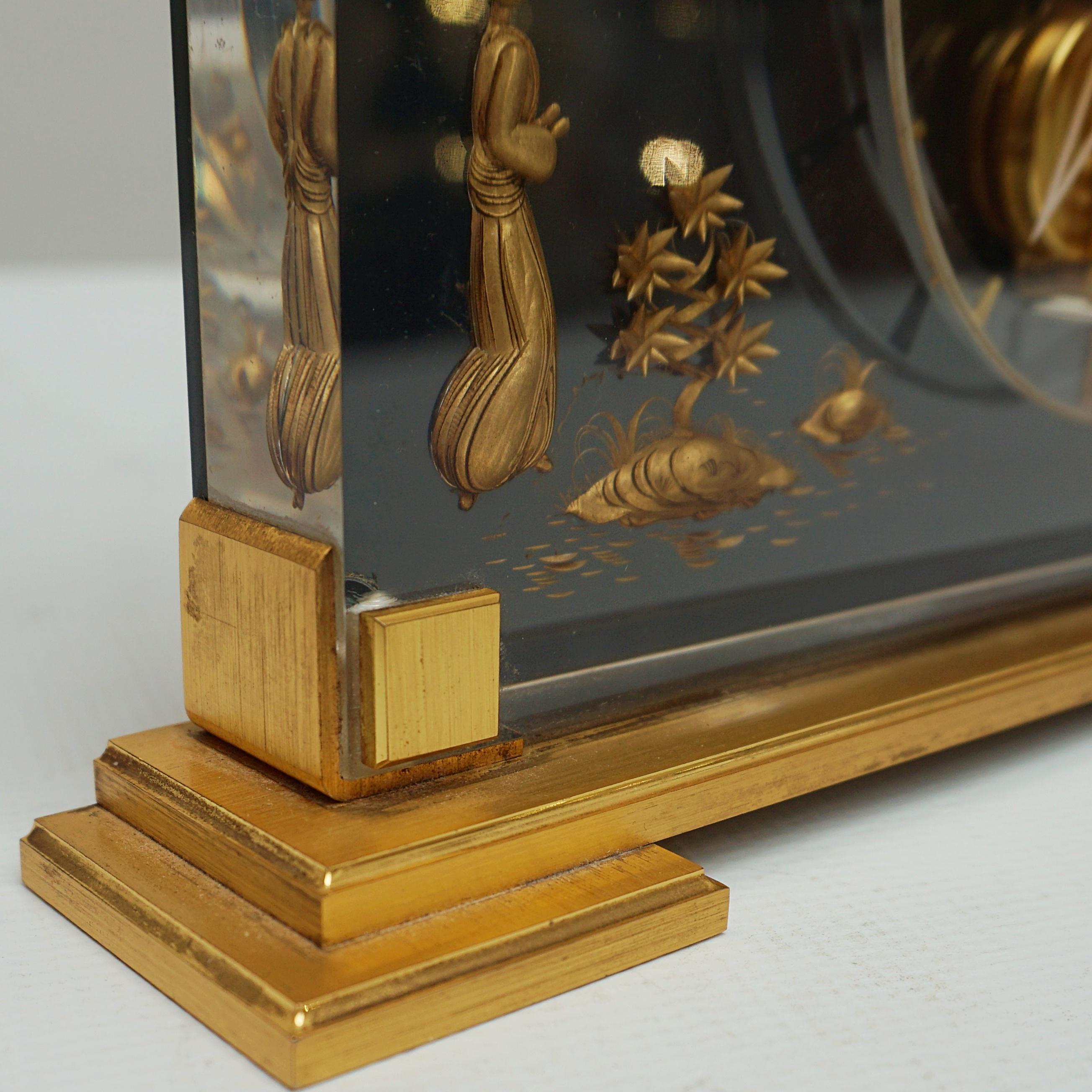 A Mid-Century Jaeger-LeCoultre mantel clock in a Lucite case with inset brass chinoiserie decoration featuring a young girl amongst the lily pads with an overhanging branch above . Set over a gilded Brass stepped base. Eight day movement by