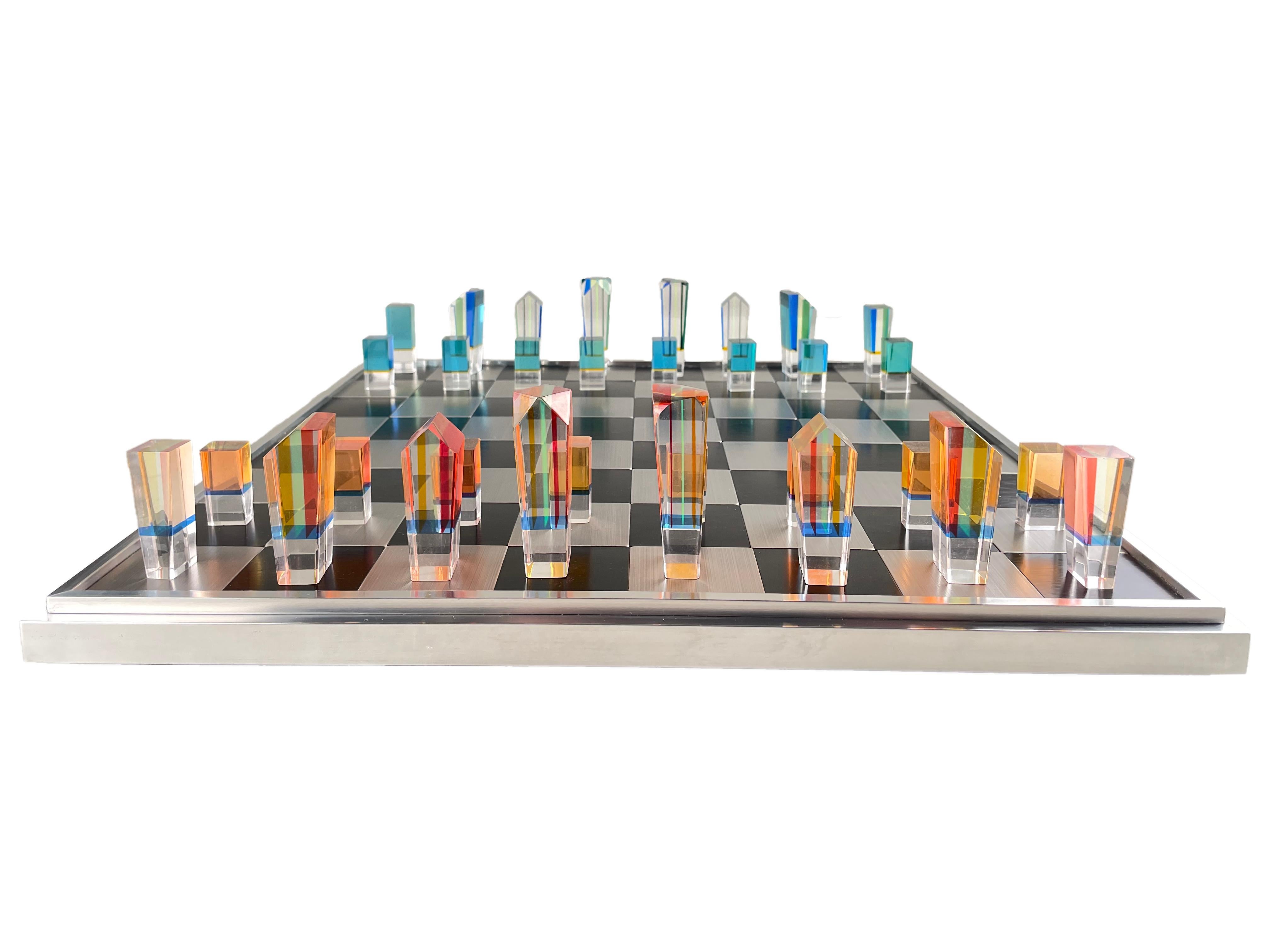 An American Mid-Century Modern acrylic and aluminum chess set by, Charles Hollis Jones with one set of pieces finished in a layered orange, yellow & red acrylic and the other pieces are yellow, blue, & green acrylic pieces together with a