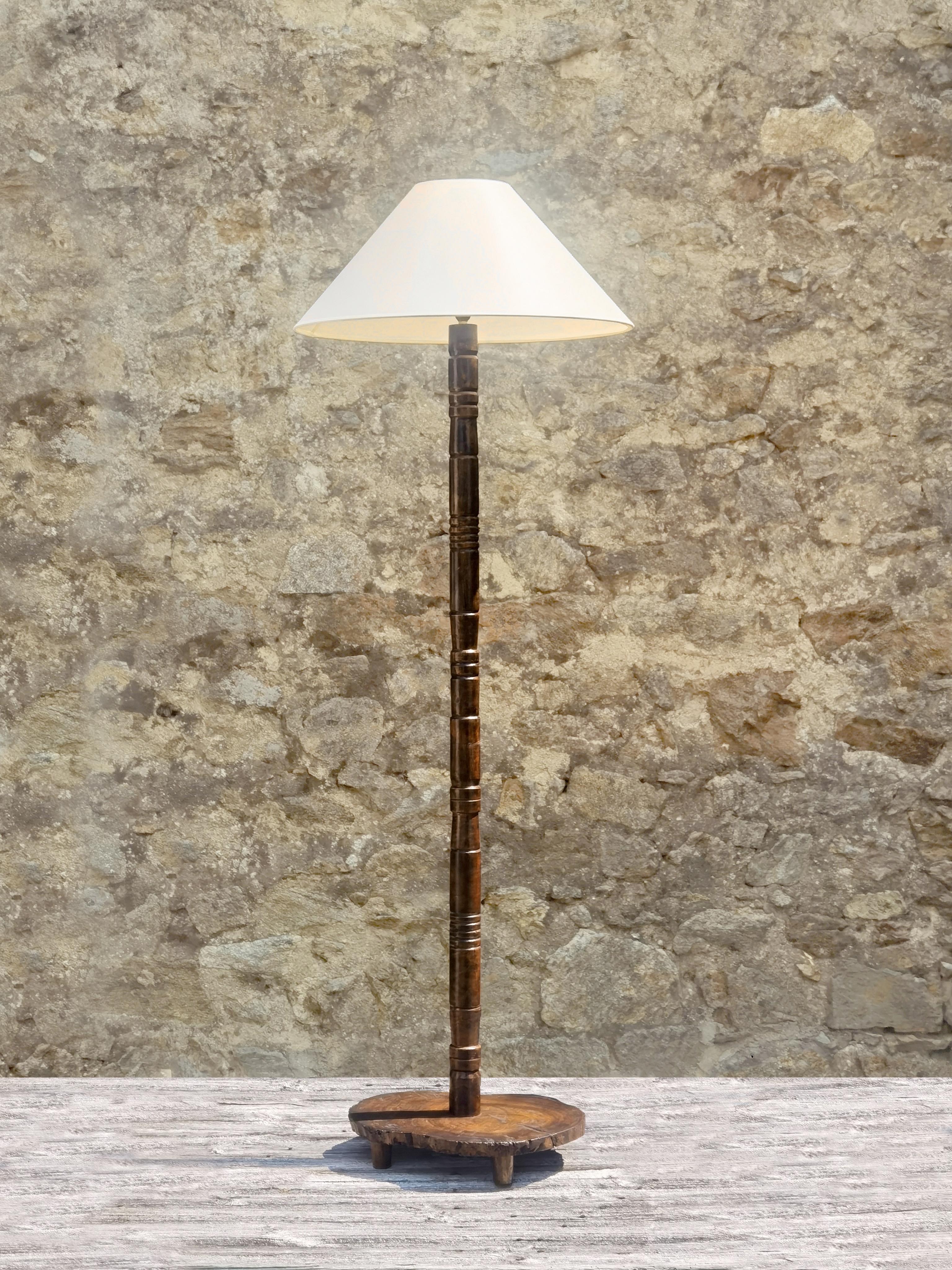 A thin, low and elegant brutalist floor lamp, Mid-Century-Modern, Modernist, Brutalist, massive tree slice base mounted on 3 wooden feets, sculptural, thin and very graphic vertical axis remembering tribal monoliths sculptures, unique piece hand