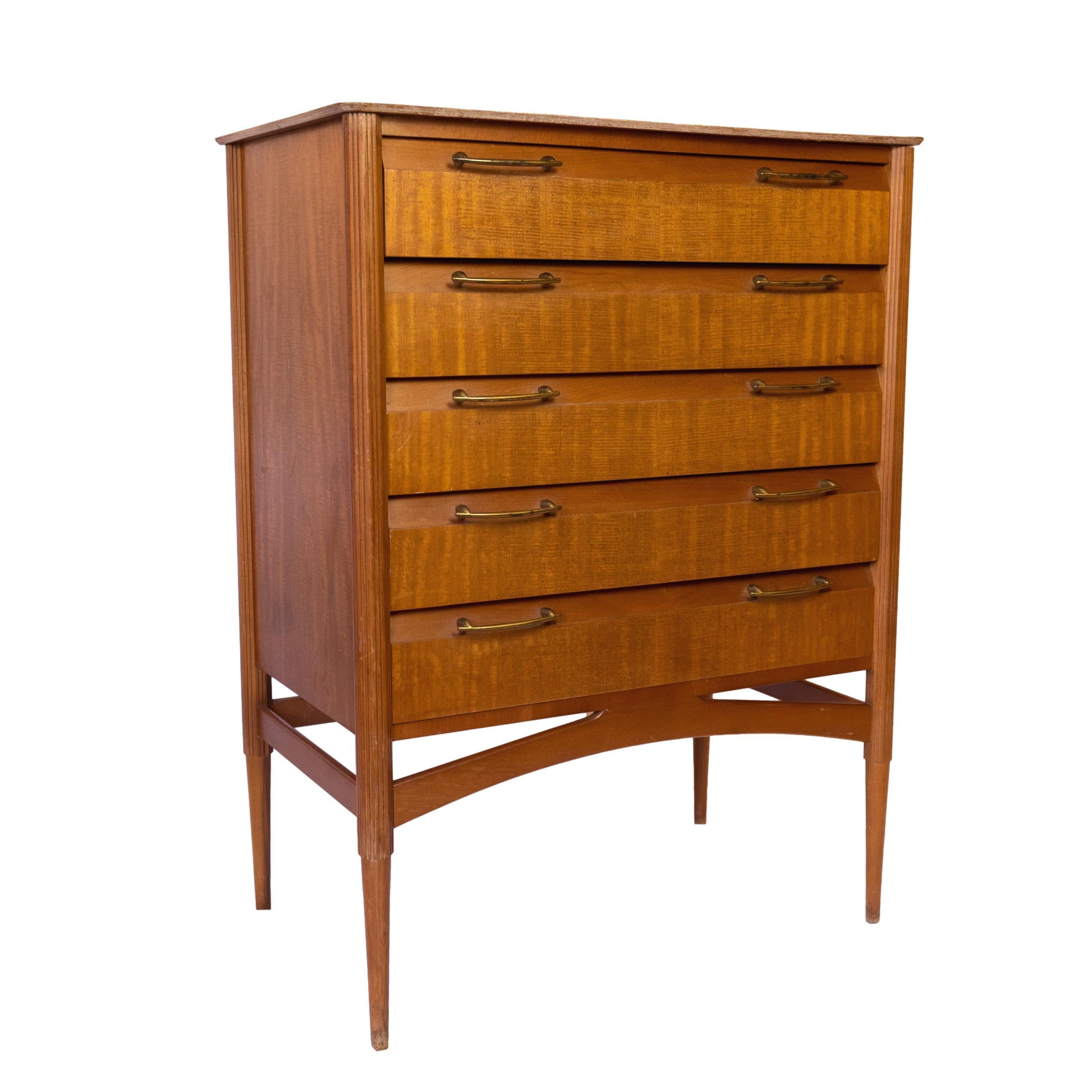 A Mid-Century Modern Flame Teak Chest-of-Drawers by Limelight, English, ca. 1965, with reeded posts and five uniform drawers, above a Danish modern stretcher, on tapered legs. 
LITERATURE:
For items in this range, see:
B. Hyman and S. Braggs,