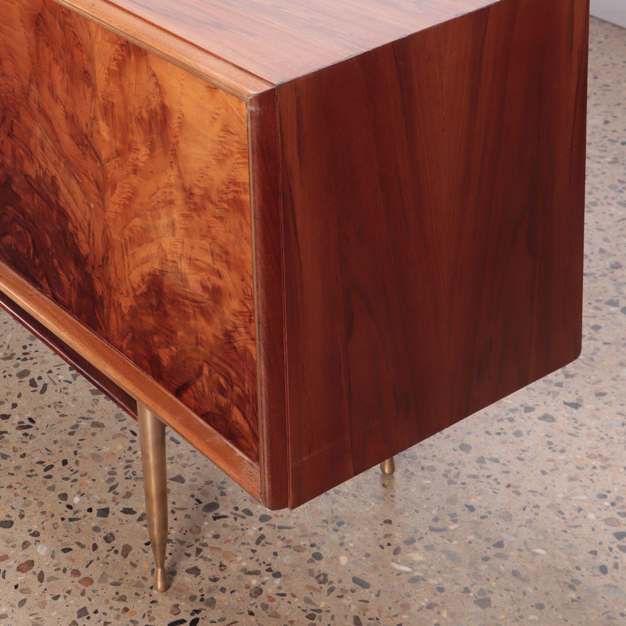 A Mid-Century Modern flame walnut sideboard having bronze trim and feet C 1960. The credenza features three central drawers flanked by two sets of doors for ample storage. Very unique exotic veneers.