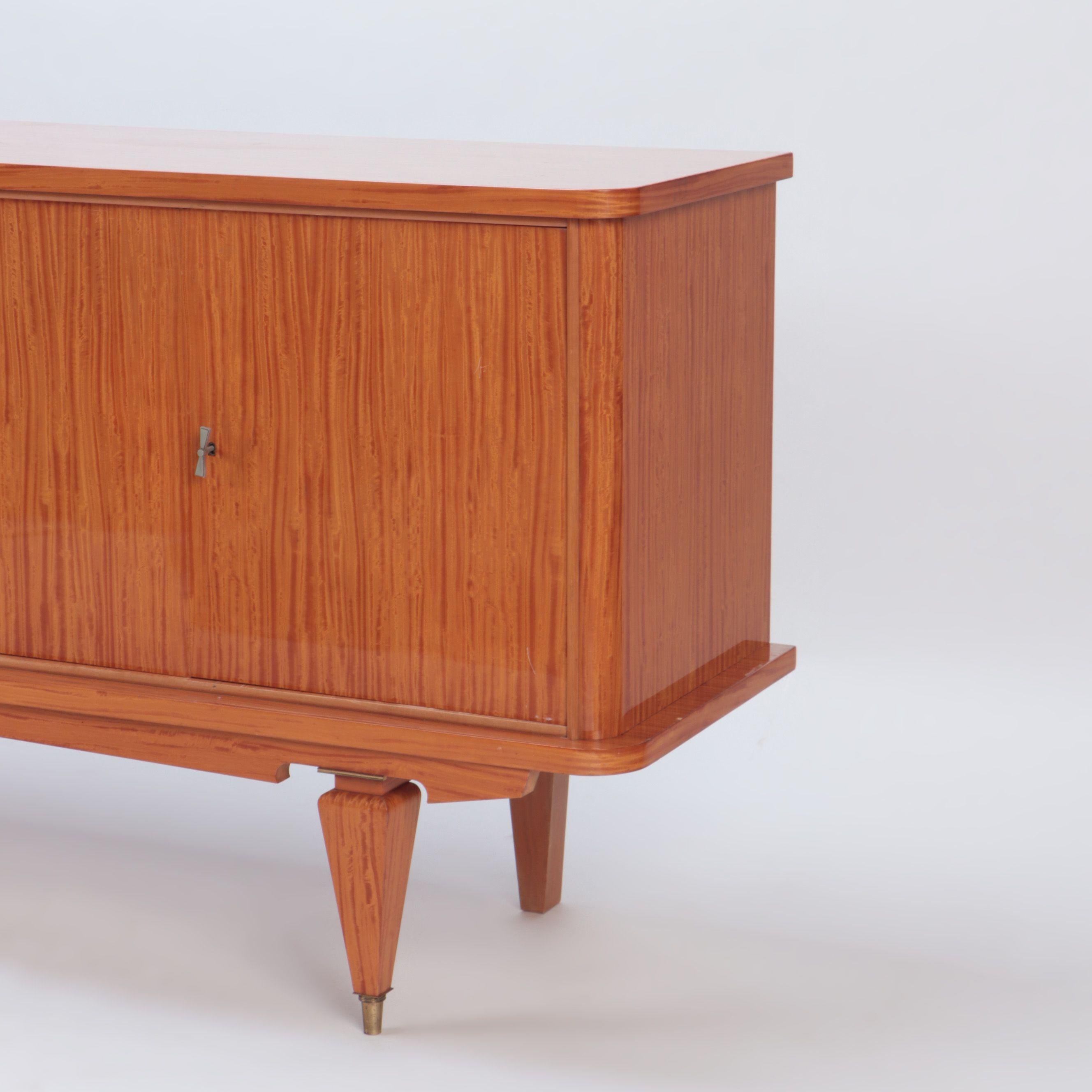 A Mid-Century Modern French two door sideboard with exotic satinwood veneers and spade feet ending in brass sabots. C 1960.