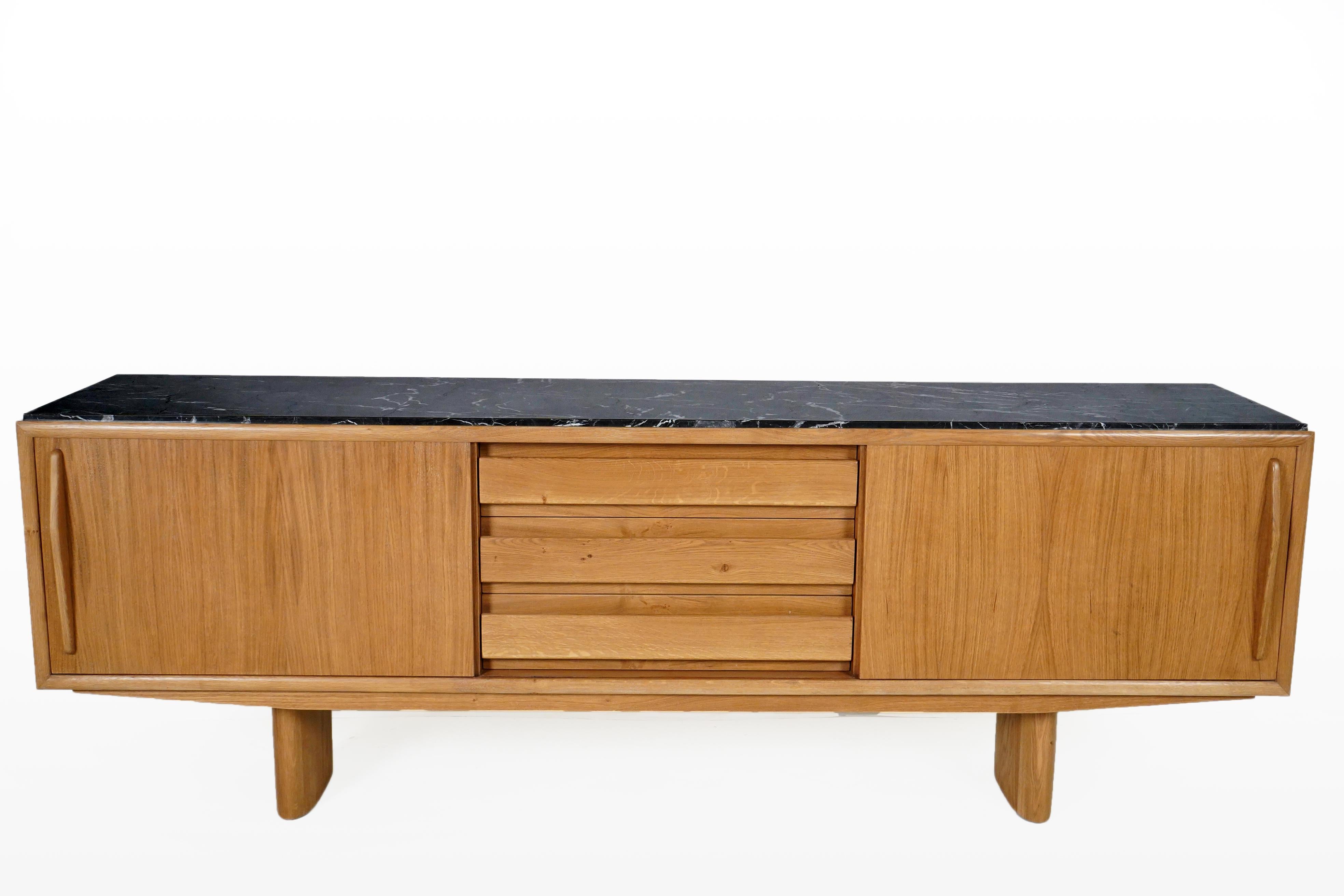 This substantial sideboard combines the beauty of straight-grained Hungarian oak and a black marble top with white veining. The case is long and lovely with two sliding doors covering ample storage bins on each side of the multi-drawered center