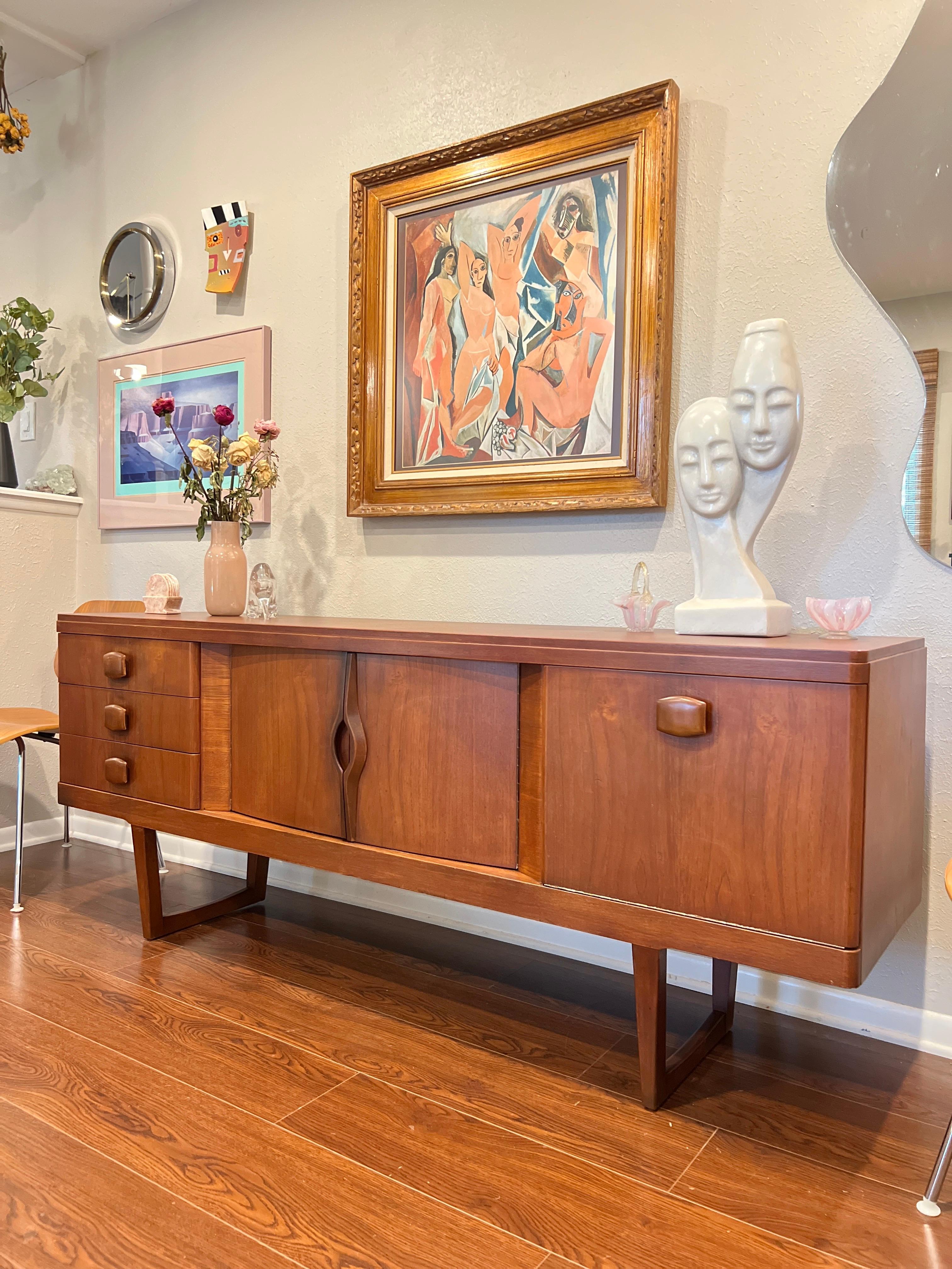 A mid century modern sideboard in teak by Stonehill, circa 1960s. This piece is on a stylish sleigh base with lots of storage space including 3 drawers, a drop door cupboard and double door cupboard. Overall, in very good vintage condition. Sturdy