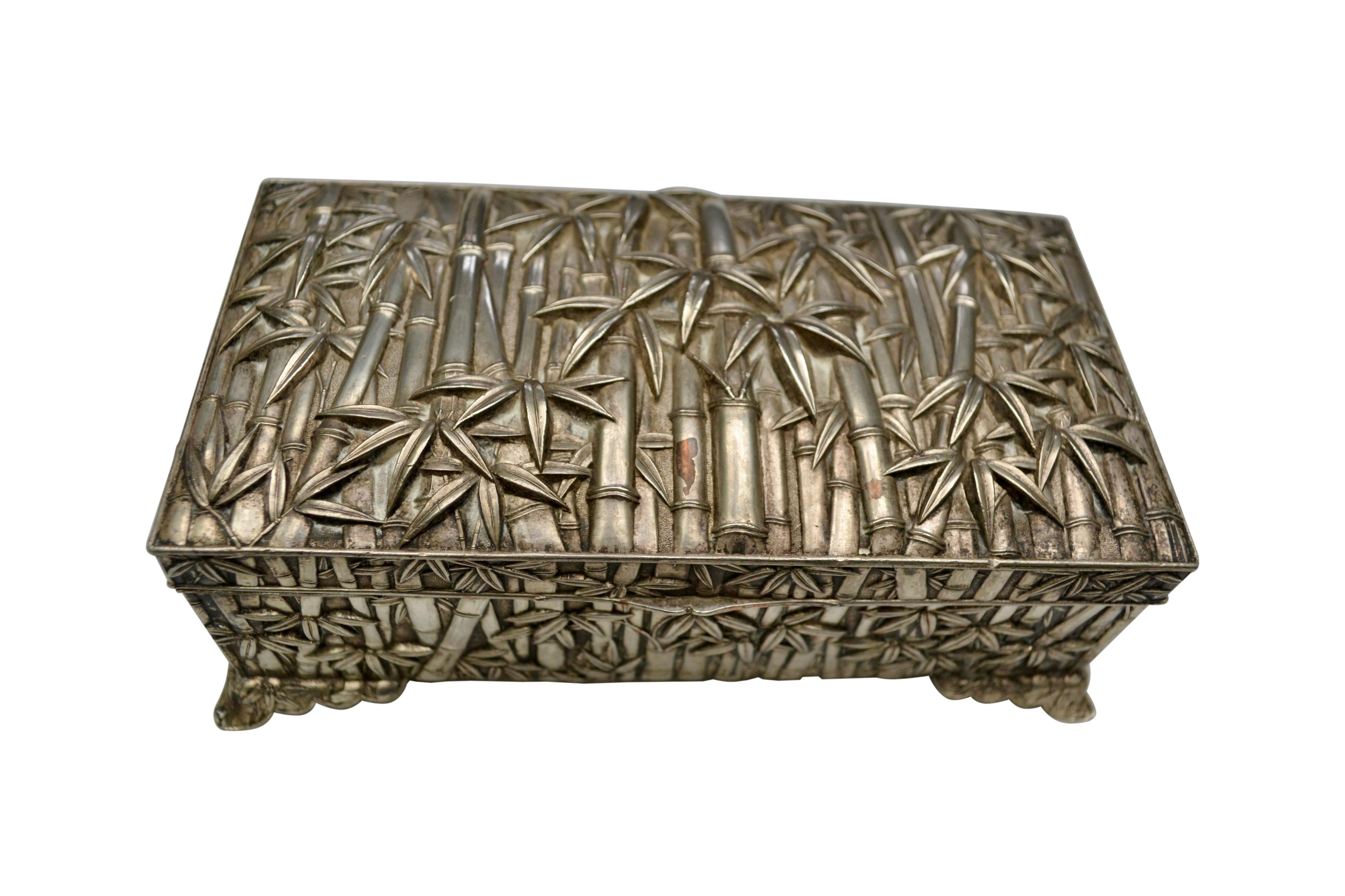 A silver plated wood lined =box with a hinged lid and stylized feet of profusely decorated with a forest of embossed bamboo trees tops. There i s a fan like hallmark on the bottom of he box.