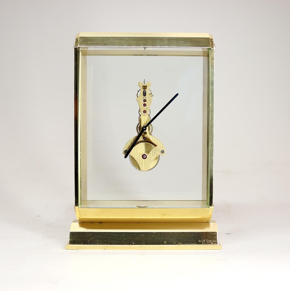 A very stylish mid-century skeleton timepiece with a gilded jeweled inline or ‘baguette’ movement suspended behind thick bevelled glass. The case is of gilded brass with a brushed and burnished finish the top and base in a contemporary faceted