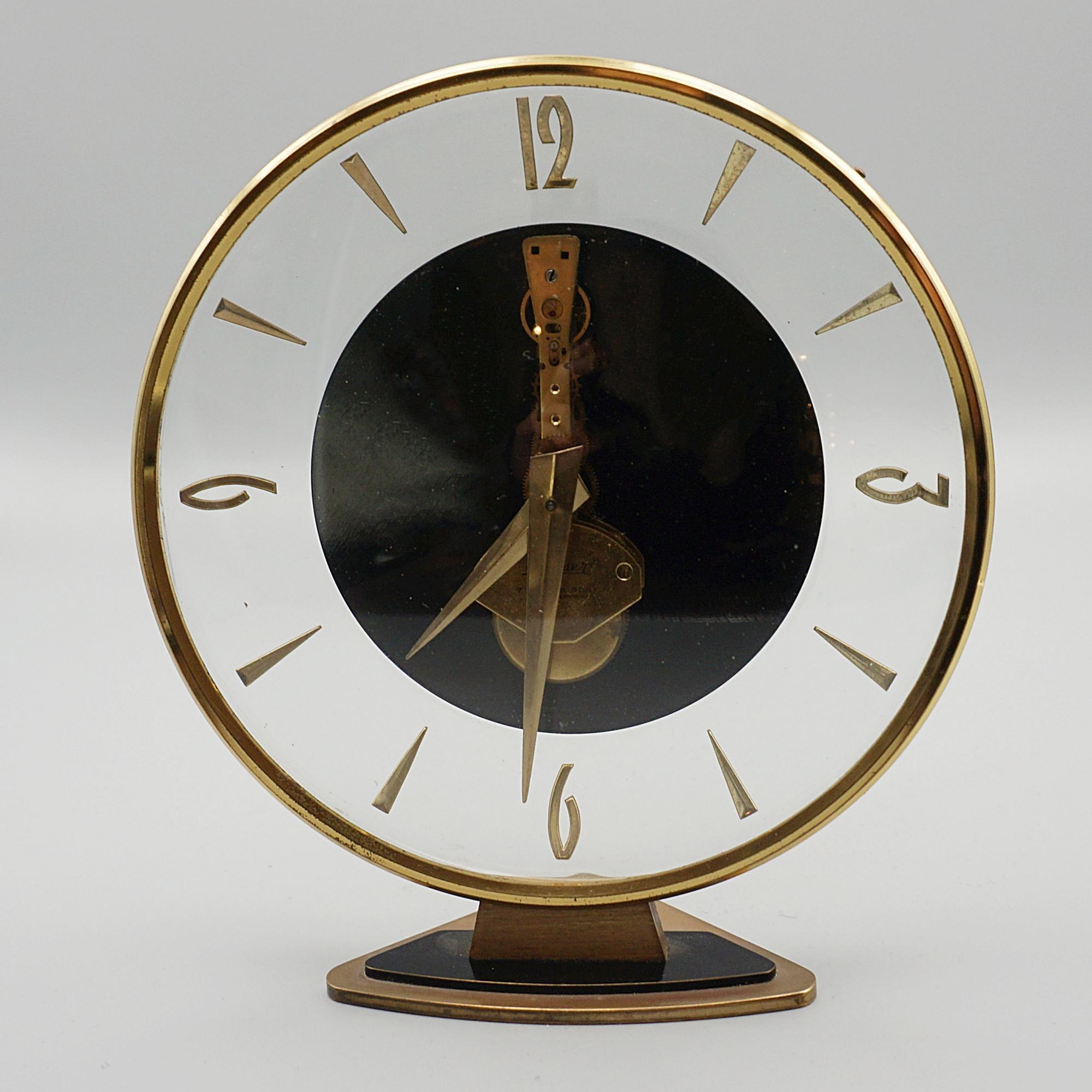 A Mid-Century table clock by Kaiser. Circular gilt brass case, with original brass hands and stylised numerals. Set over a triangular gilded brass base with 'Kaiser' etched to dial. Original 8 day movement, in full working order.

Dimensions: H 17cm