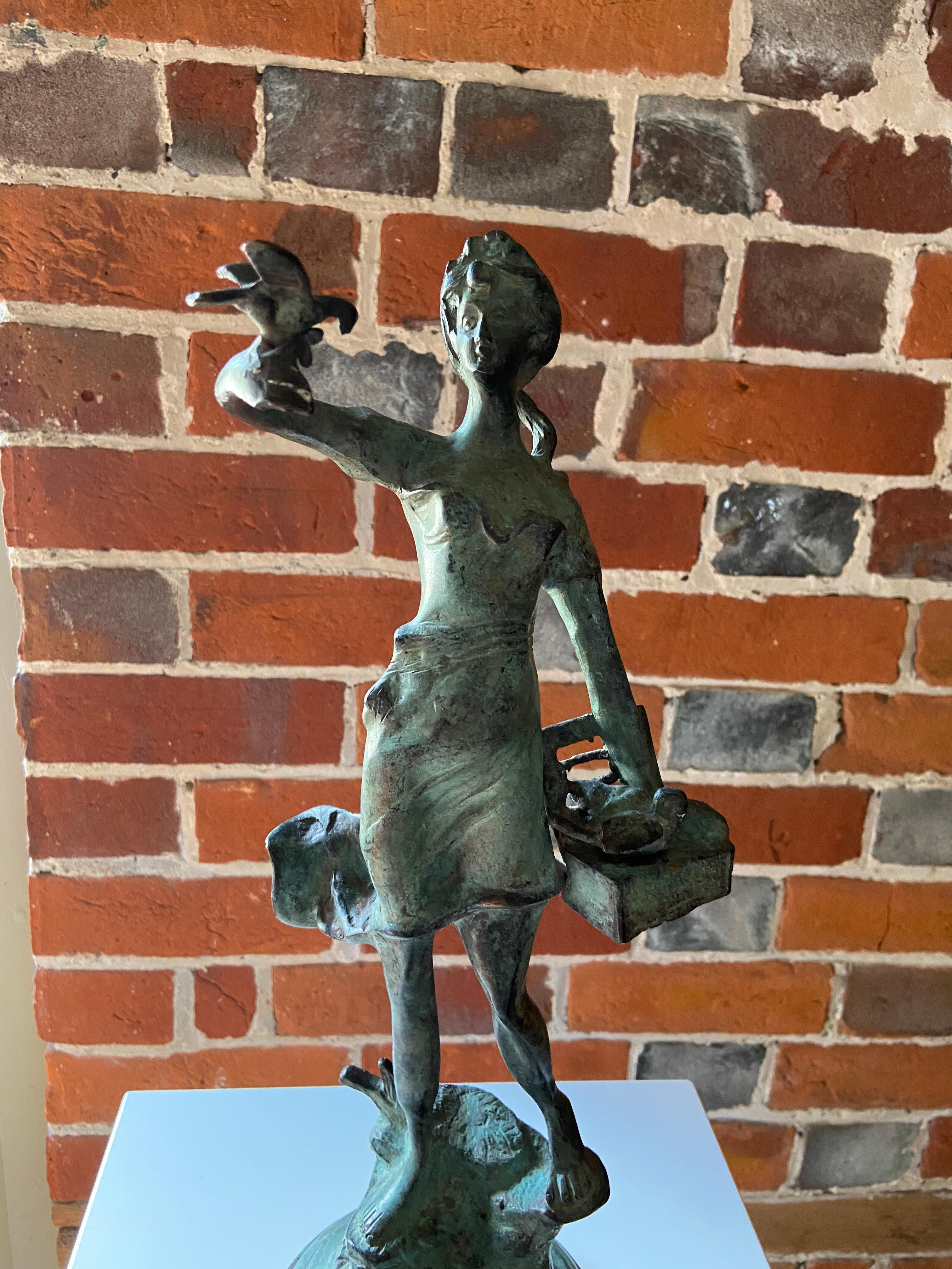 A stylised mid-century verdigris bronze figure of a girl releasing doves from a box, stood on a naturalistic base. The piece is unsigned but would date to the 1960s and is likely to be Italian. Figurative sculpture of this period would often show